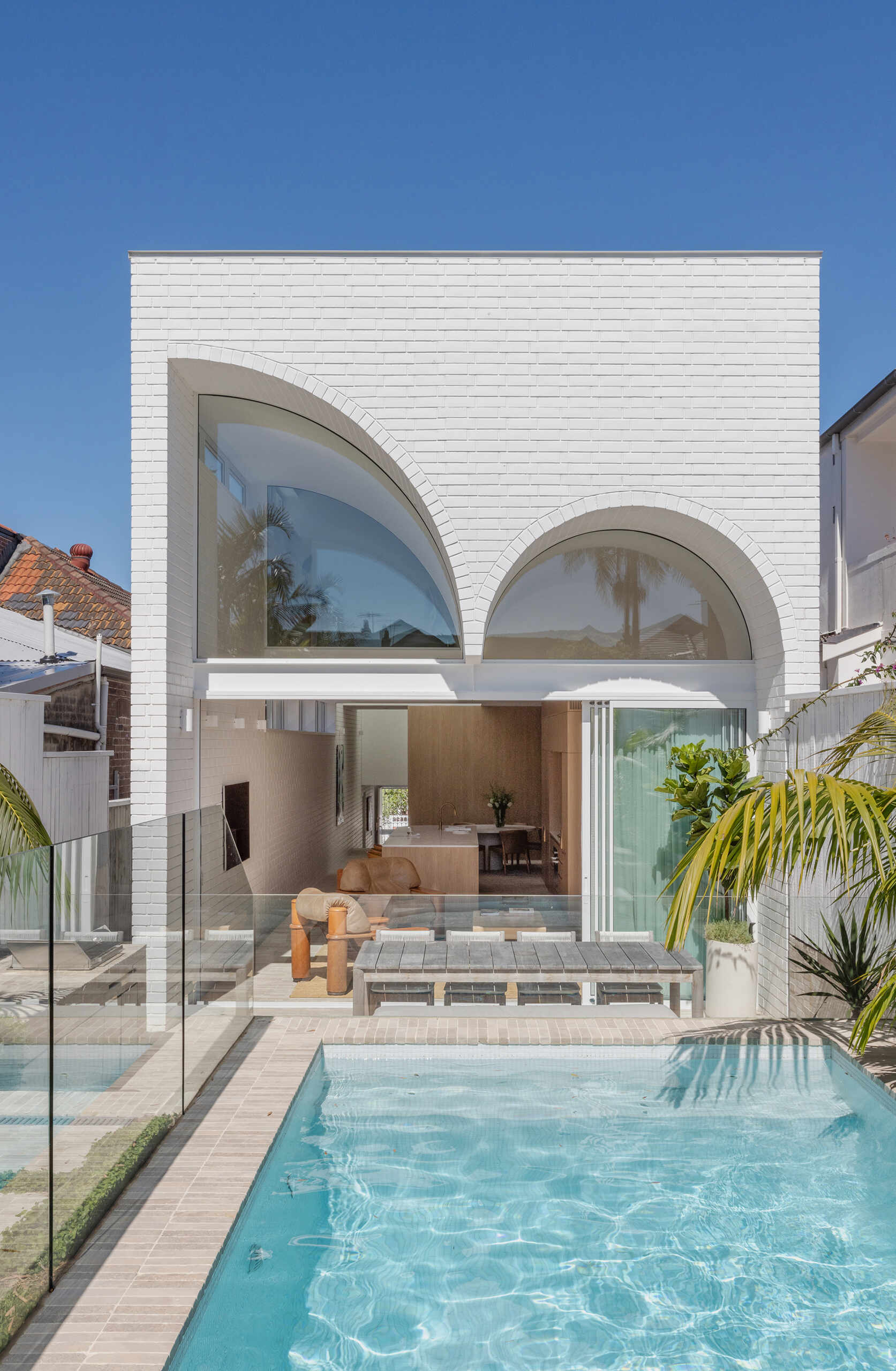Above the living area, the ceiling expands into two soaring curves. These forms define the rear of the house. Here, the curves are pressed into the solid brick mass. They appear weighty and monumental, reversing the lighter expression seen at the front of the home.