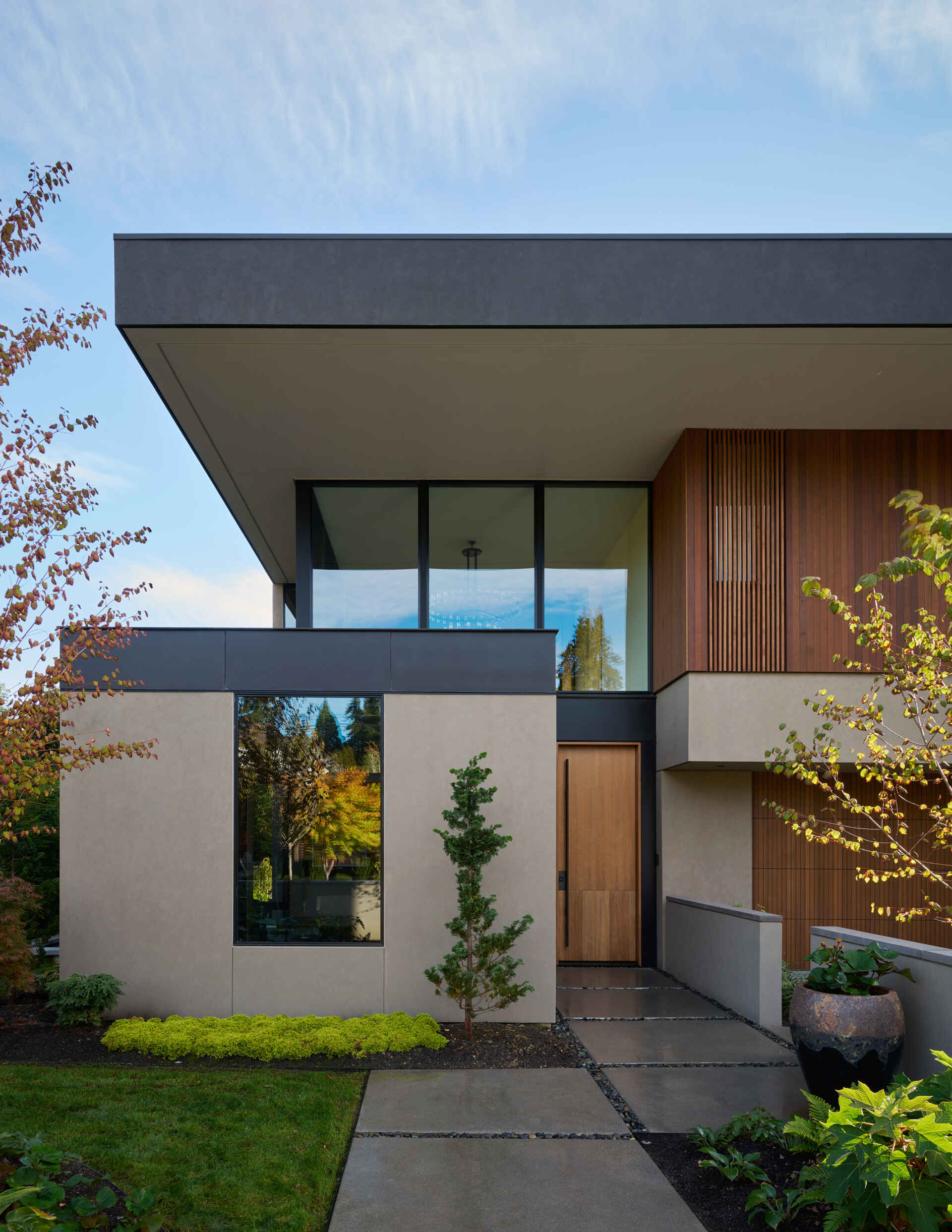 This modern home blends Pacific Northwest style with Thai-inspired wood screens. Sleek glass, steel, and warm walnut create a bright, inviting exterior.