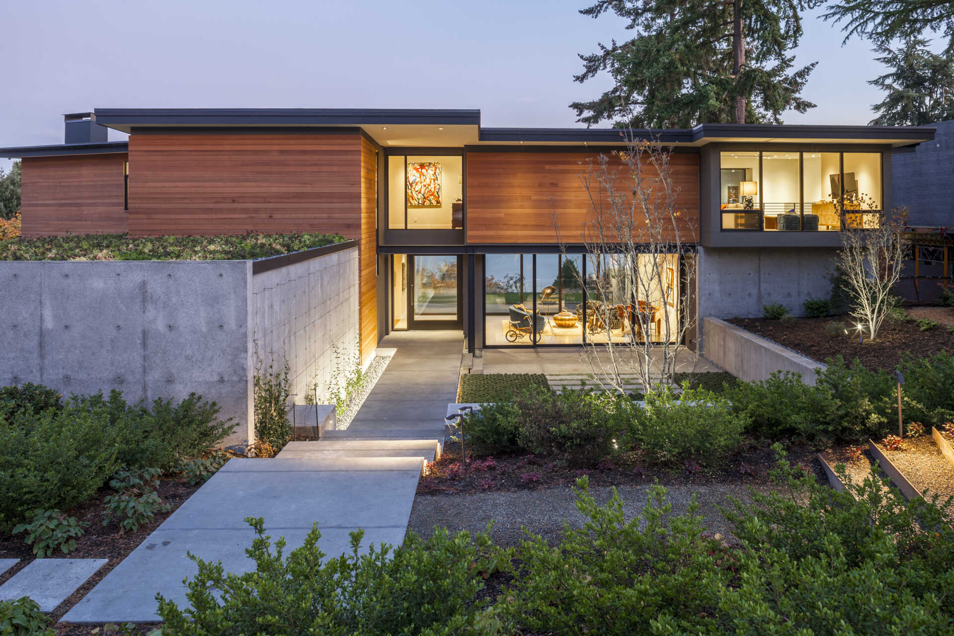 A landscaped courtyard carved into the hillside leads to an oversized pivot door, creating a calm transition from street to home.