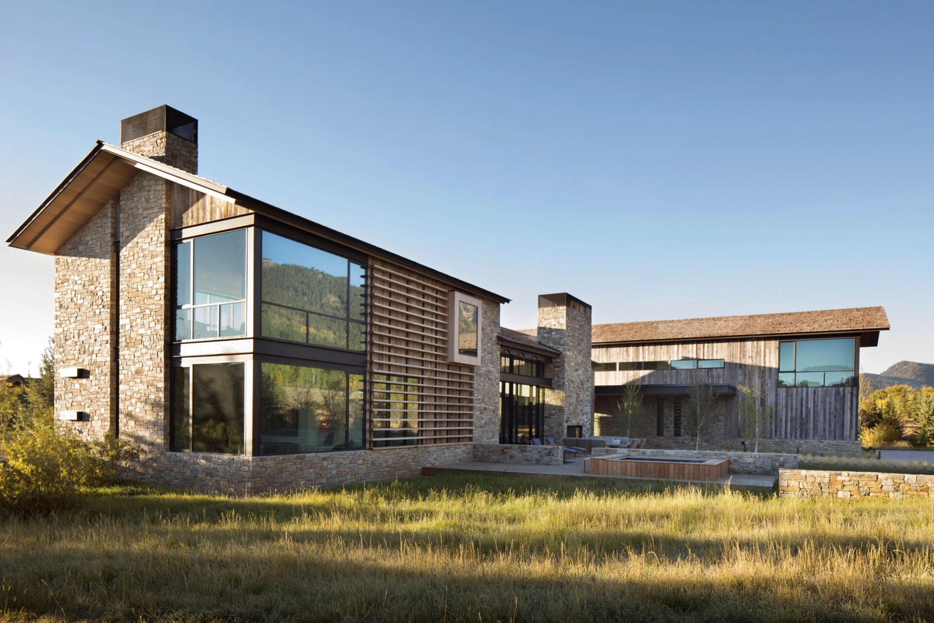 Las tejas de cedro, los aleros extendidos y la piedra rústica le dan a esta casa de Wyoming durabilidad y textura mientras se mezclan con su entorno montañoso.