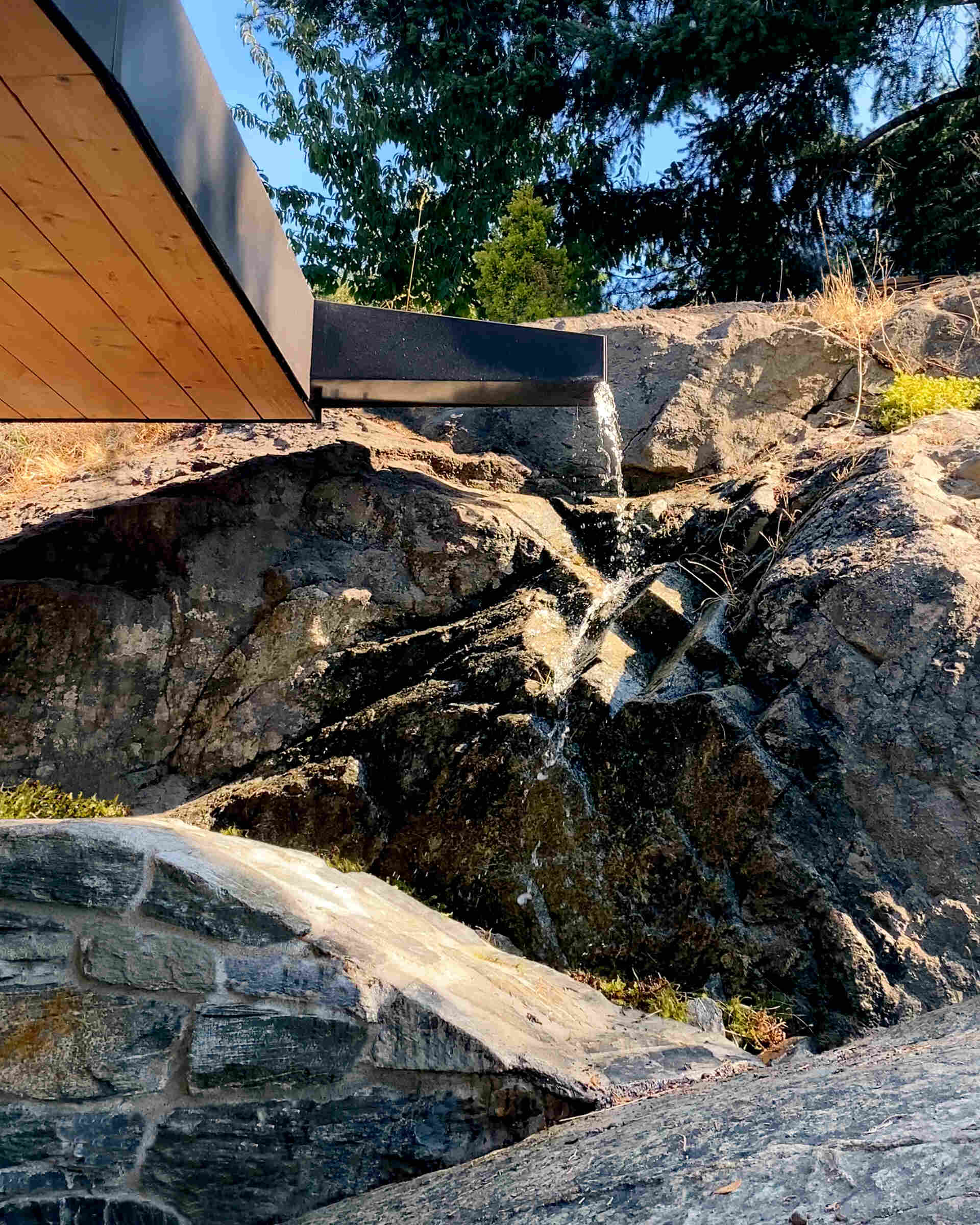Rainwater is directed to splash onto the rock below, amplifying sound and later recycled to extend the experience through dry summer months.