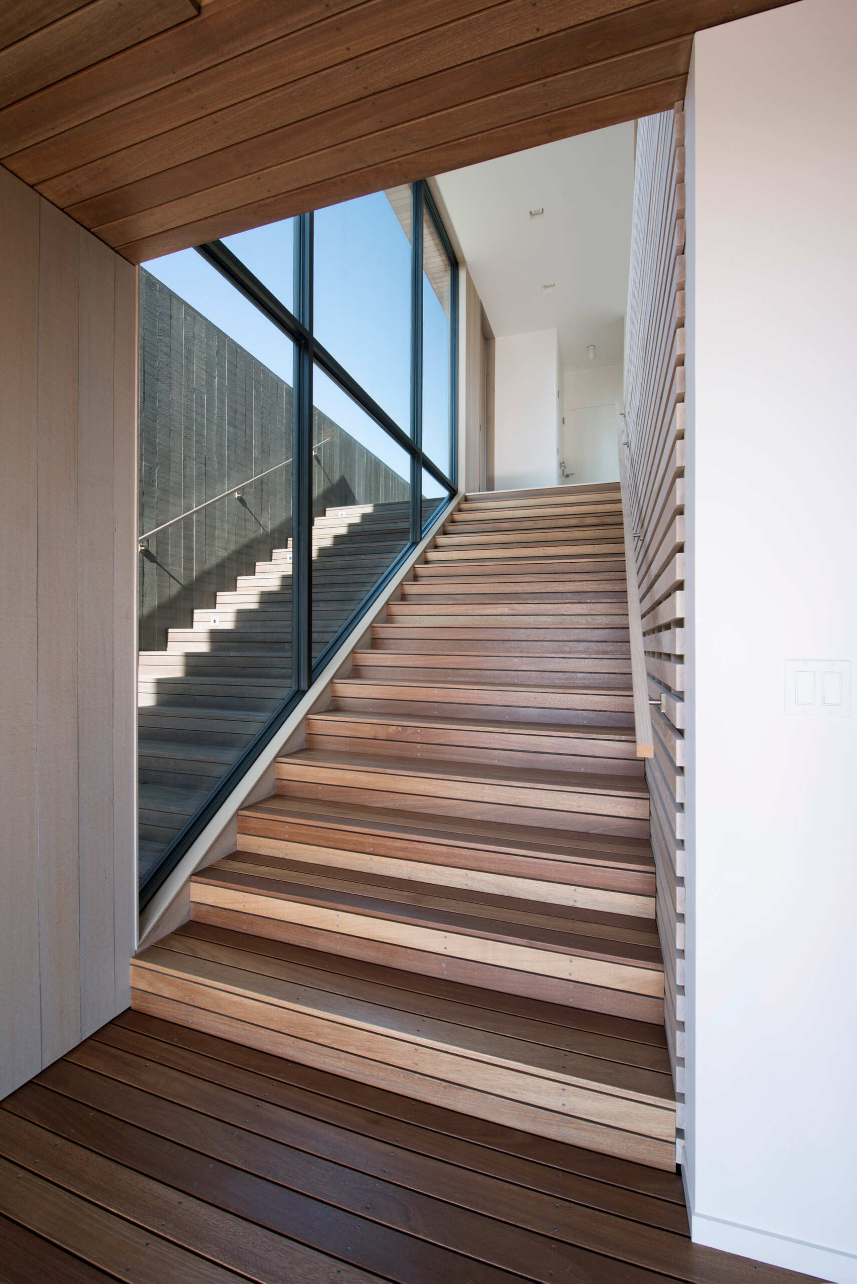 Una moderna escalera de madera en una casa frente al mar está revestida con un muro de contención de madera y piedra azul.