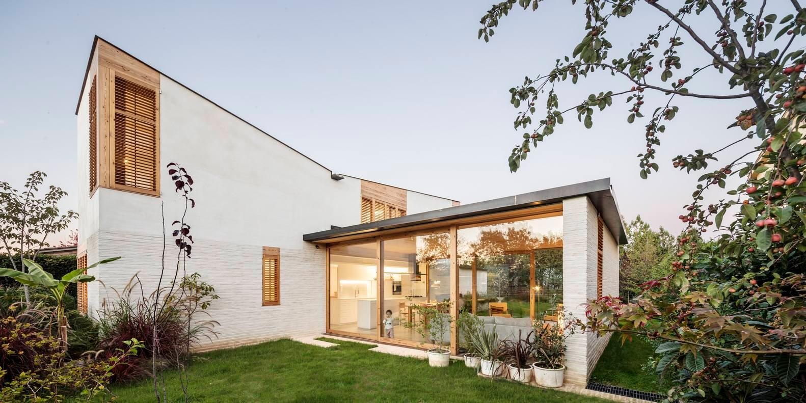 Un volumen horizontal transparente forma el corazón de la casa, con paredes corredizas de vidrio que se abren a los jardines a ambos lados.