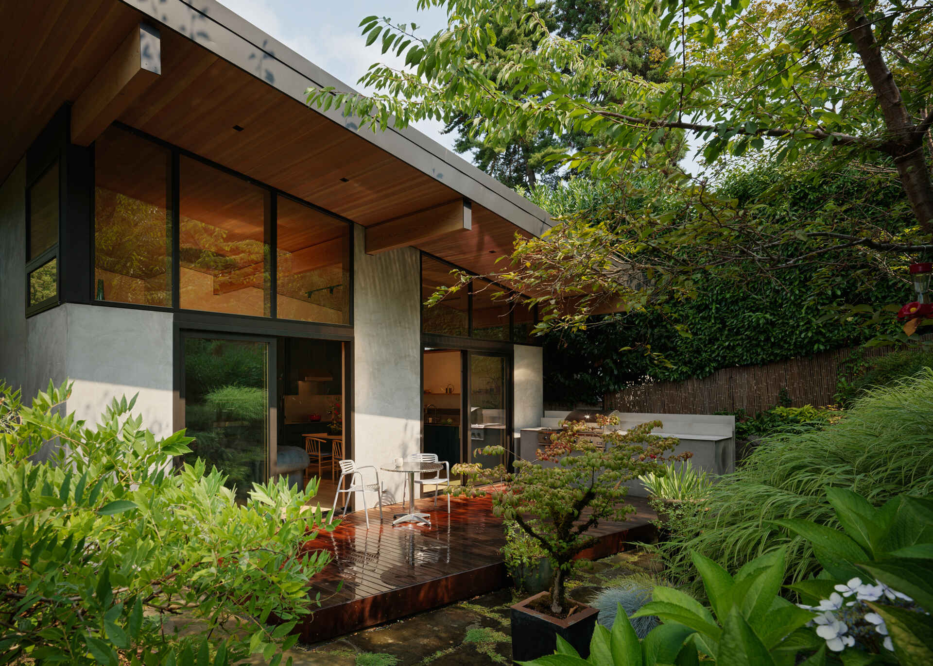 The south-facing patio flows from the main living area through large lift-and-slide doors. An outdoor kitchen extends the social spaces, and the layered northwest garden provides a lush backdrop. The design encourages indoor-outdoor living in the Pacific Northwest climate.