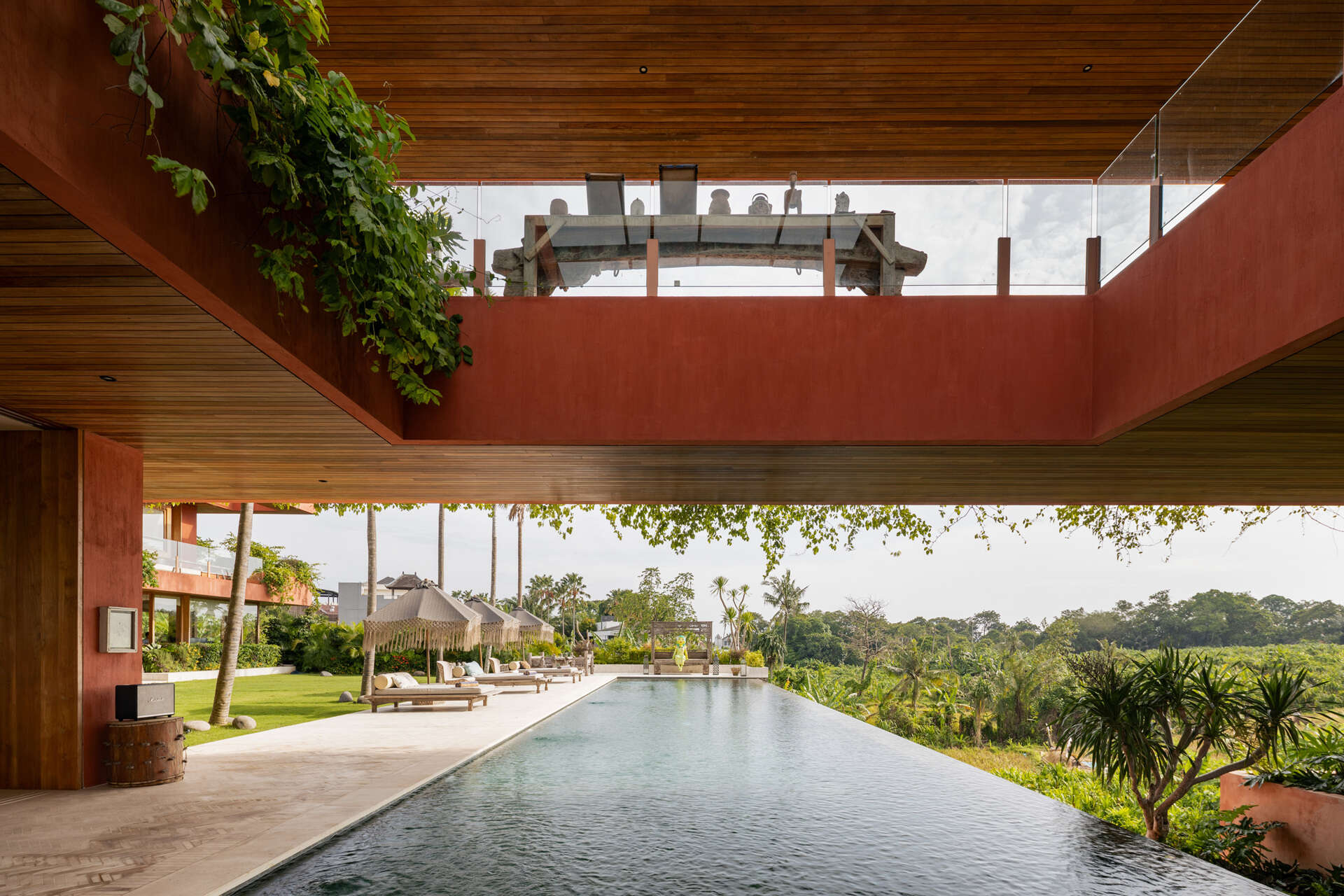 An oversized swimming pool stretches along the front of the house, opening uninterrupted views toward surrounding rice fields.