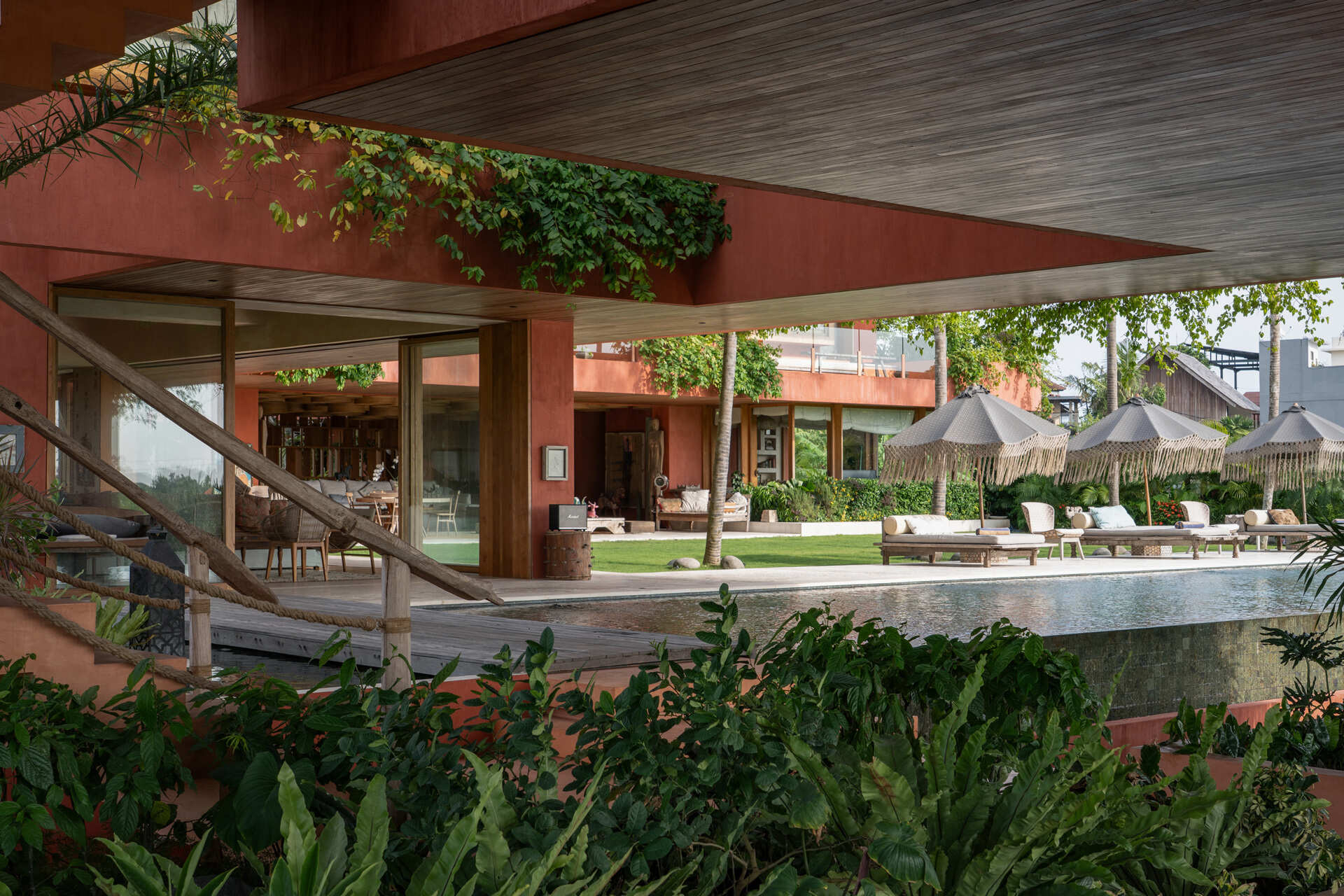 An oversized swimming pool stretches along the front of the house, opening uninterrupted views toward surrounding rice fields.