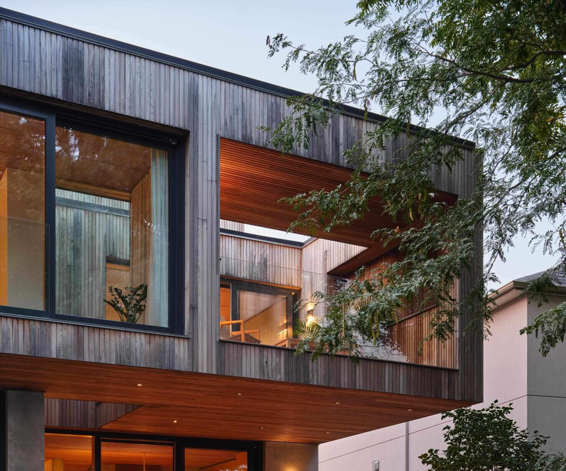 Looking back toward the house, subtractions carved from the wood volume reveal layered interior and exterior spaces. The rear facade faces south, pairing open views with shaded decks that respond to changing light conditions throughout the day.