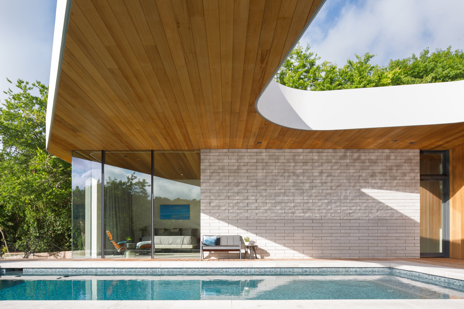 Los recortes en el techo, una piscina y una plataforma de madera definen el espacio exterior en la parte trasera, con vista al paisaje natural más allá.