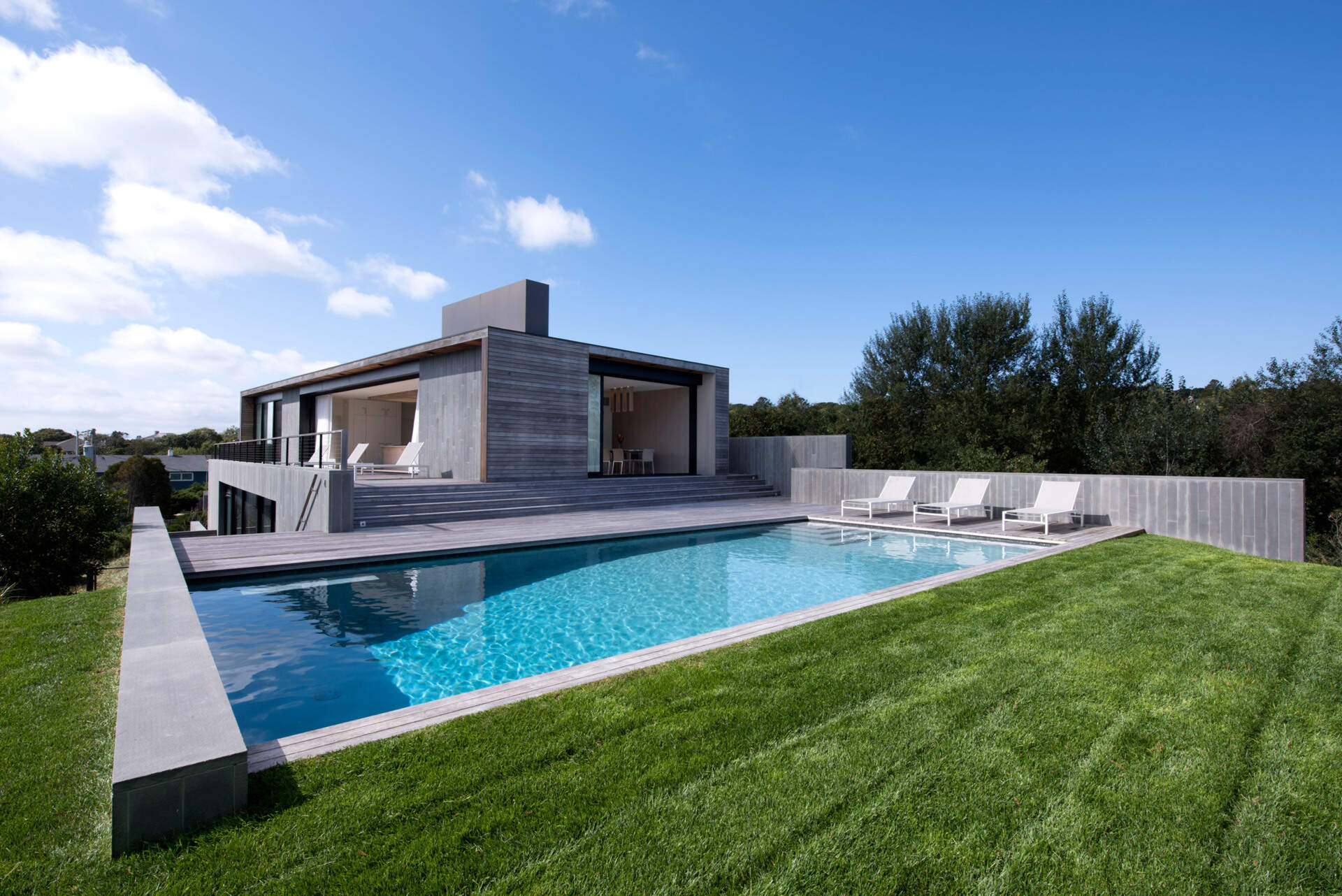 Las terrazas siguen la pendiente natural del sitio hasta la piscina y el césped, reforzando la conexión de la casa con el paisaje.