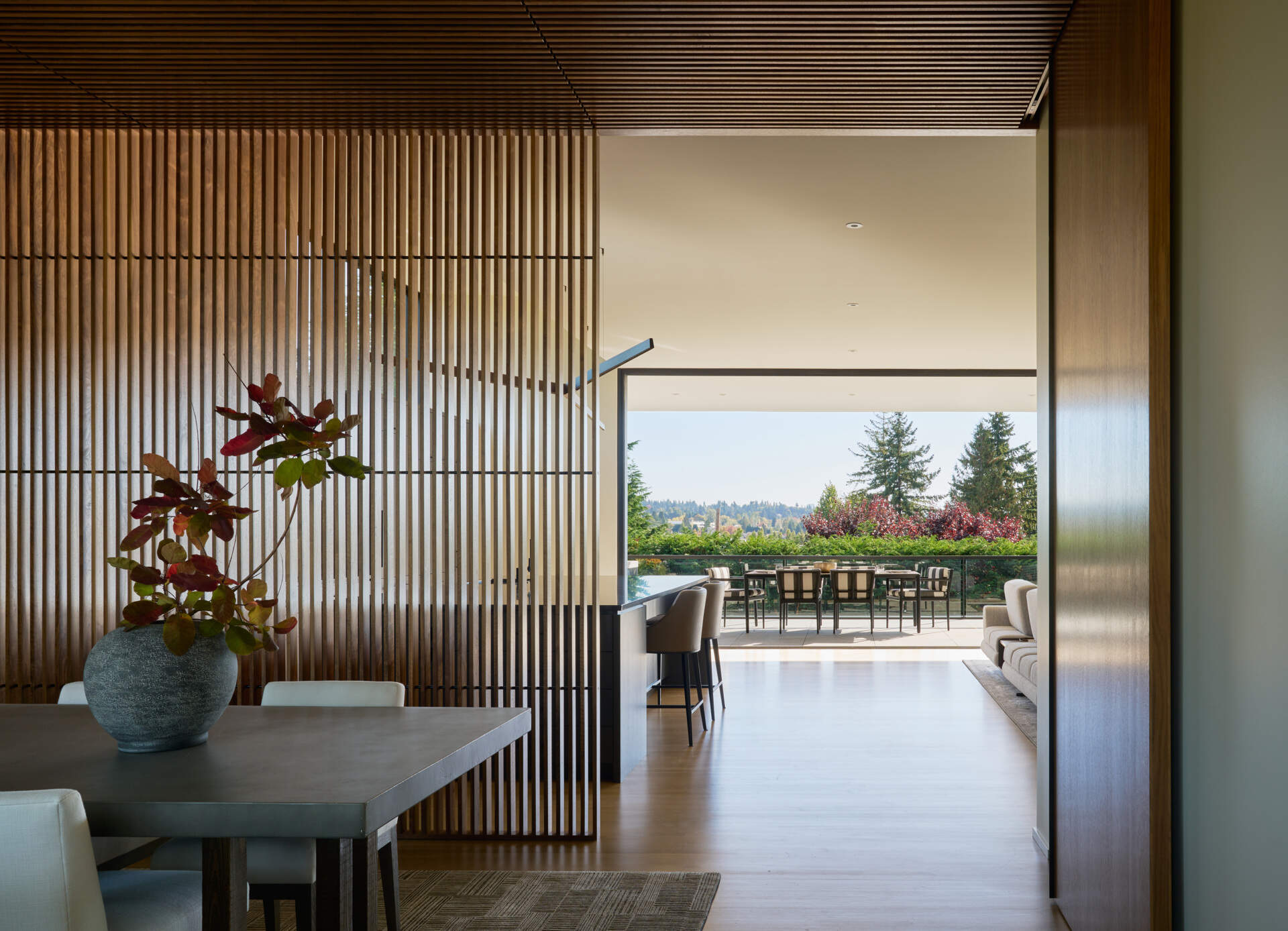 Light floods the entry, anchored by a floating staircase that casts patterned shadows. Neutral furnishings and tactile finishes balance warmth and minimalism.