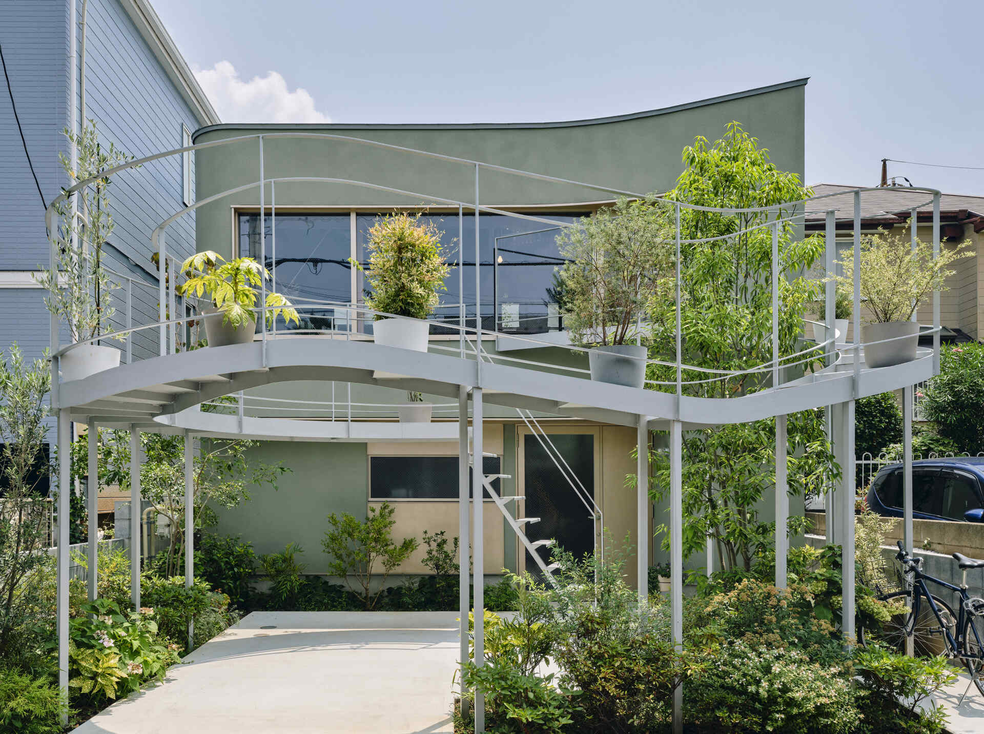 A curved second floor garden extends toward the street, catching light and creating a soft boundary between home and city in a dense Tokyo neighborhood.