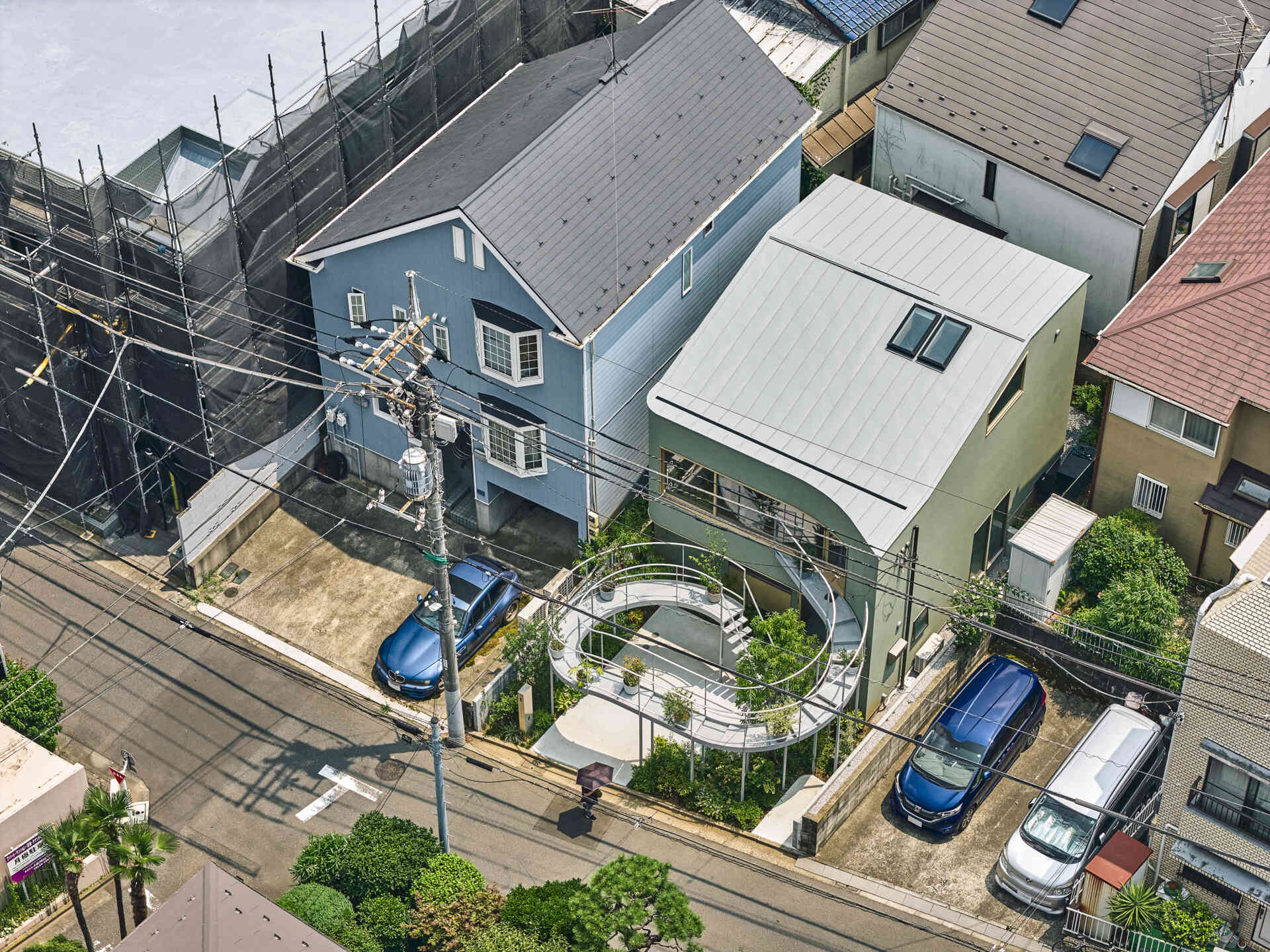 A curved second floor garden extends toward the street, catching light and creating a soft boundary between home and city in a dense Tokyo neighborhood.