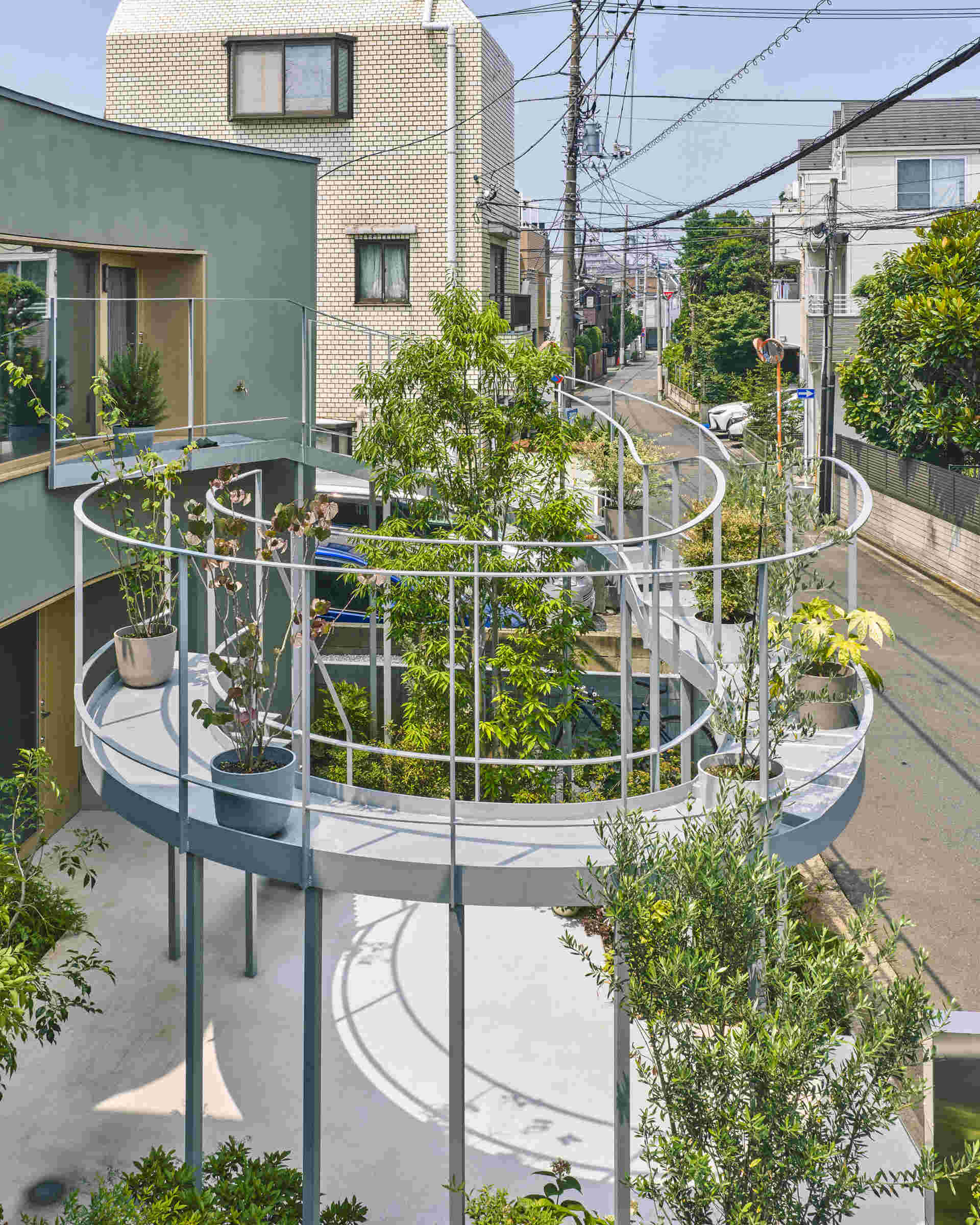 A curved second floor garden extends toward the street, catching light and creating a soft boundary between home and city in a dense Tokyo neighborhood.