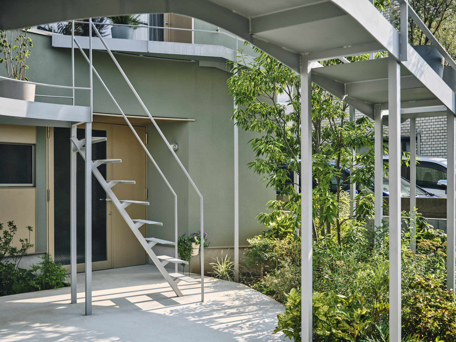 A curved second floor garden extends toward the street, catching light and creating a soft boundary between home and city in a dense Tokyo neighborhood.