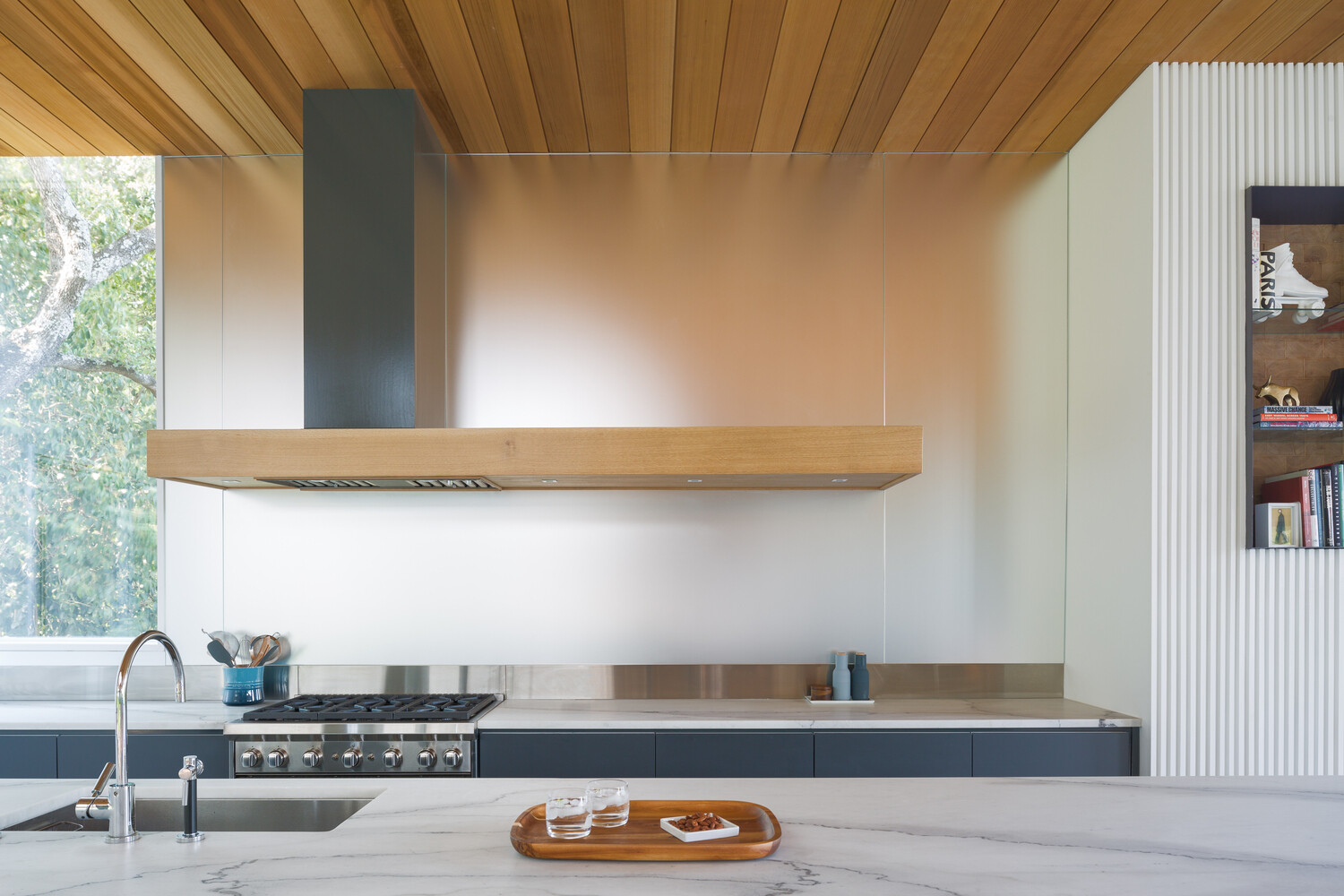 Los gabinetes oscuros y el protector contra salpicaduras de metal agregan contraste a la cocina, equilibrando materiales sofisticados con la funcionalidad cotidiana.