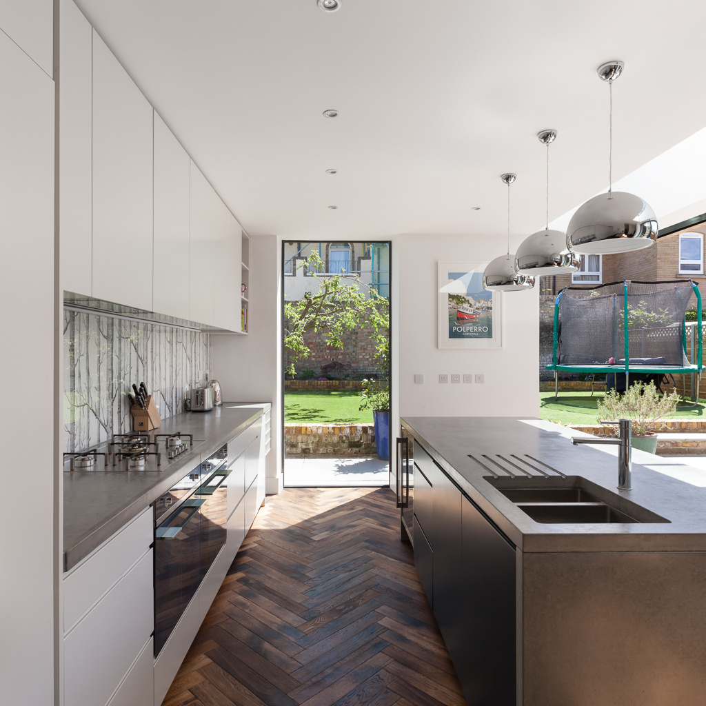 En esta cocina, las encimeras de hormigón, un protector contra salpicaduras de estilo natural y una lámpara colgante pulida añaden textura y contraste.