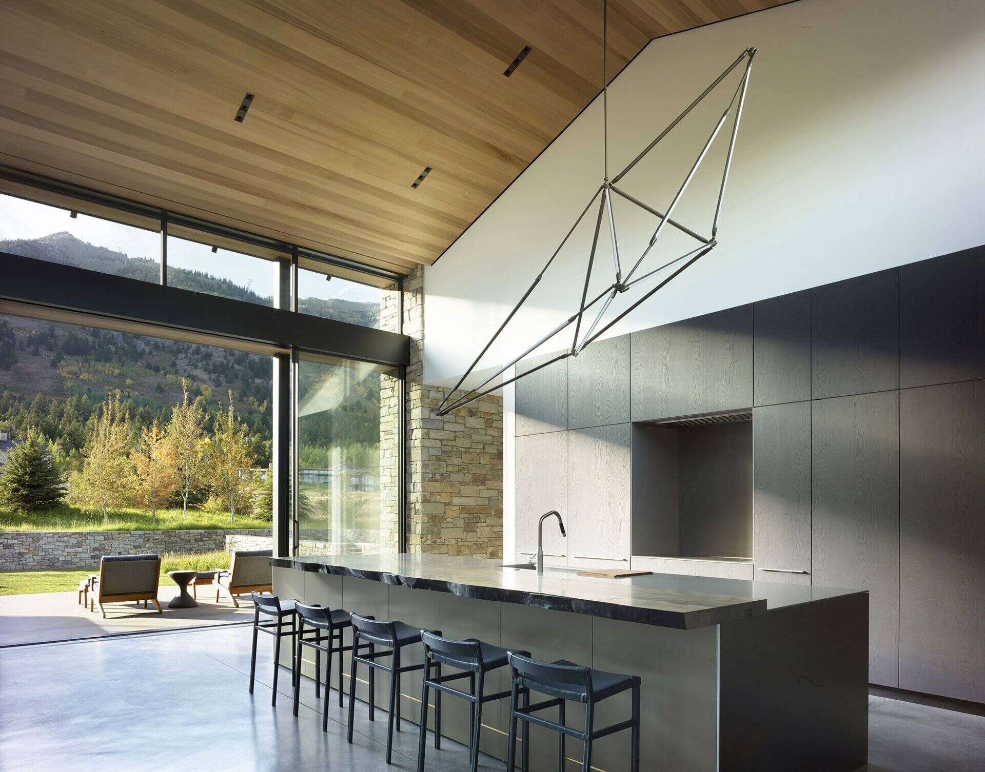 Los sencillos gabinetes oscuros y una gran isla contrastan con el techo de madera y las paredes blancas de esta moderna cocina de montaña.