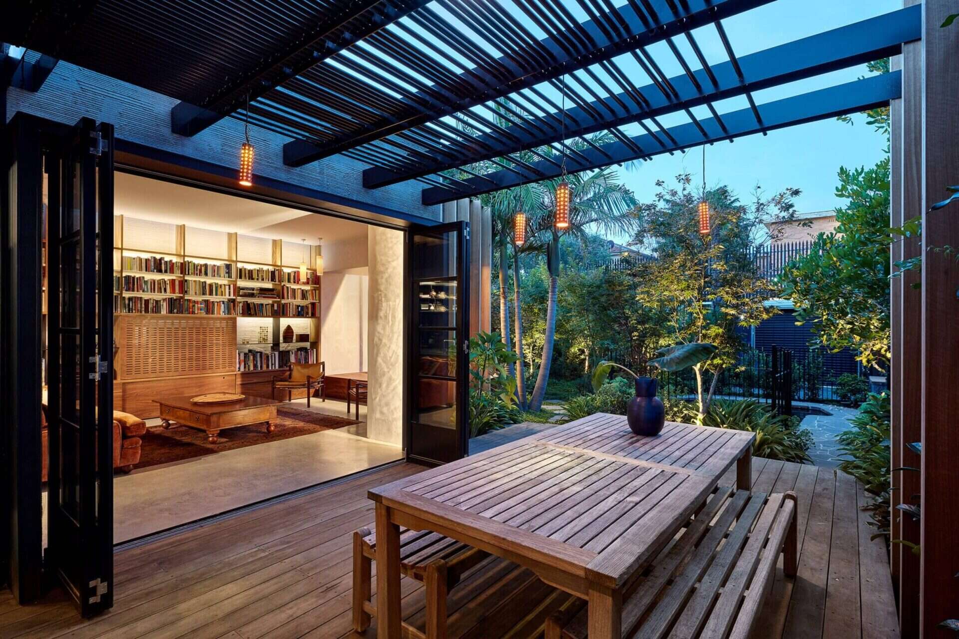 Folding glass doors connect the living room to a deck, extending the interior outward. This deck links via stepping stones to a second outdoor platform at the end of the living room, as well as to a small swimming pool. These outdoor areas are treated as extensions of the interior rather than separate zones.