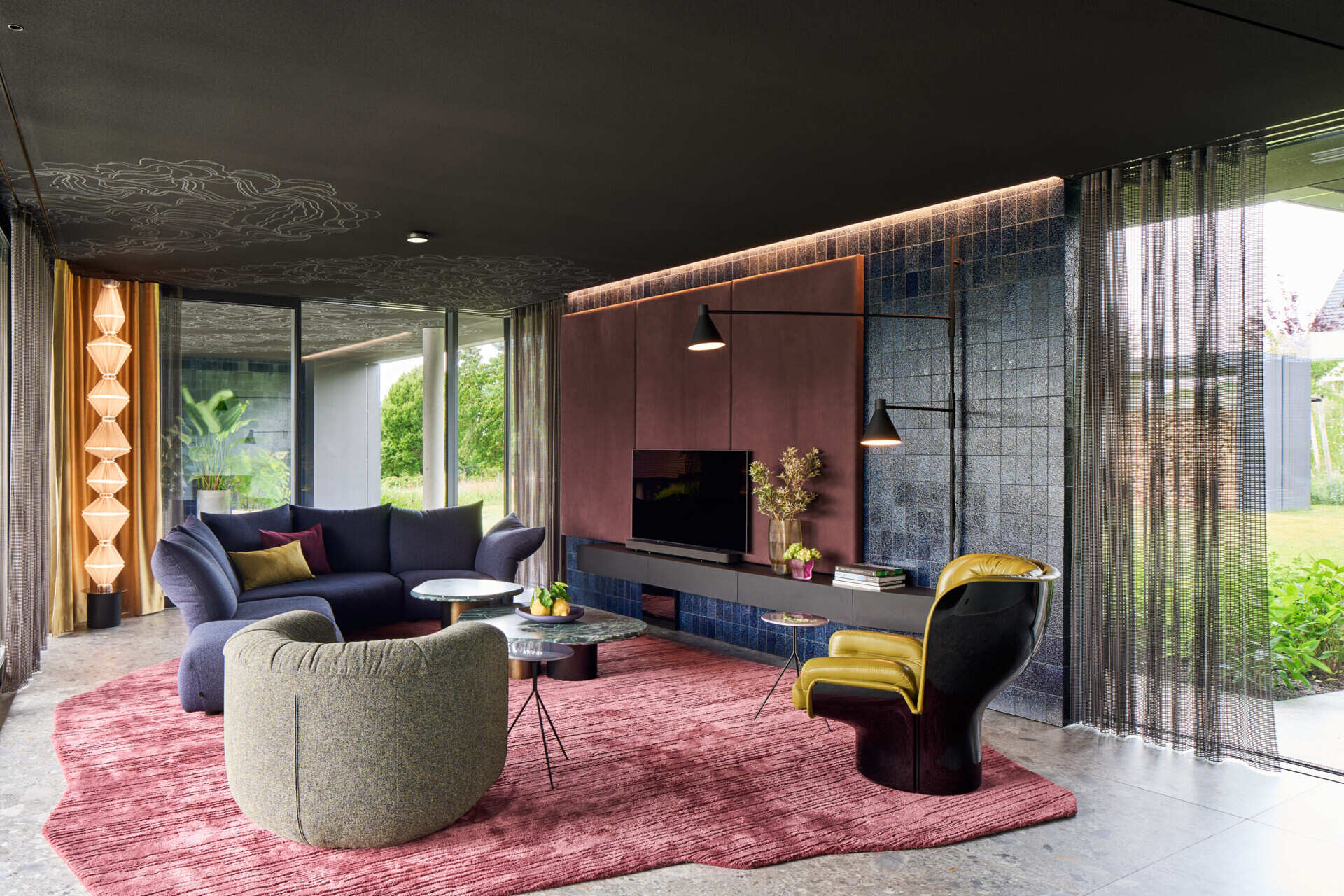 In this living room, a black ceiling stretches across the space, immediately setting the tone. It allows color and material to step forward, turning furniture and sculptural objects into characters within the room. Each element stands on its own, yet remains part of a carefully balanced composition.