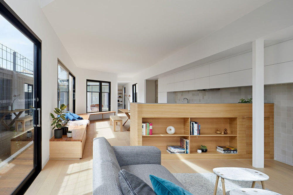 A low timber wall with open shelving separates kitchen and living areas while keeping the space open and connected.