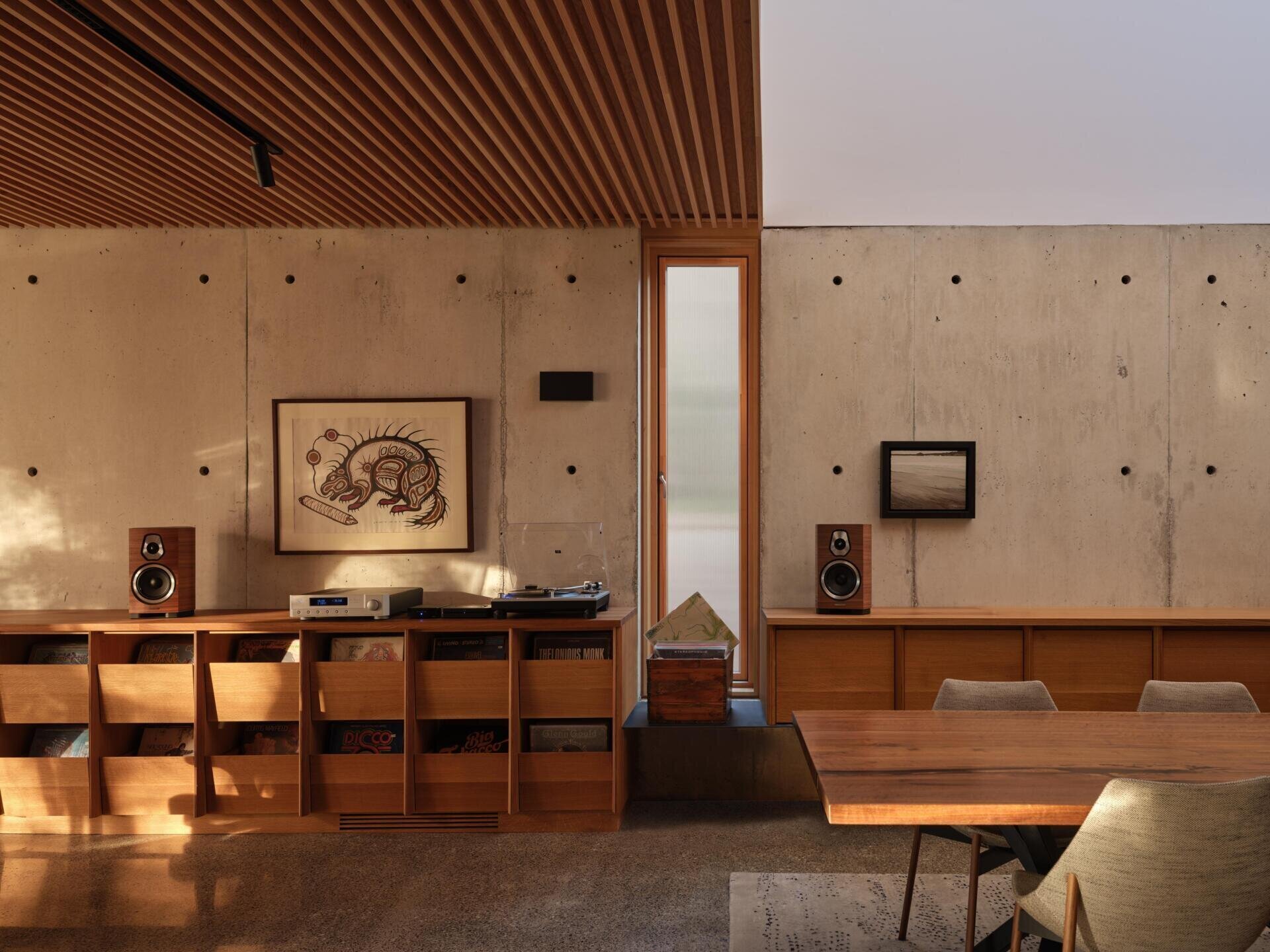 This modern living room opens west toward the lake, framed by millwork cabinets along the wall which house a custom vinyl record storage unit, while a window aligns precisely with the acoustic ceiling, reinforcing the sense that every element has been carefully measured.
