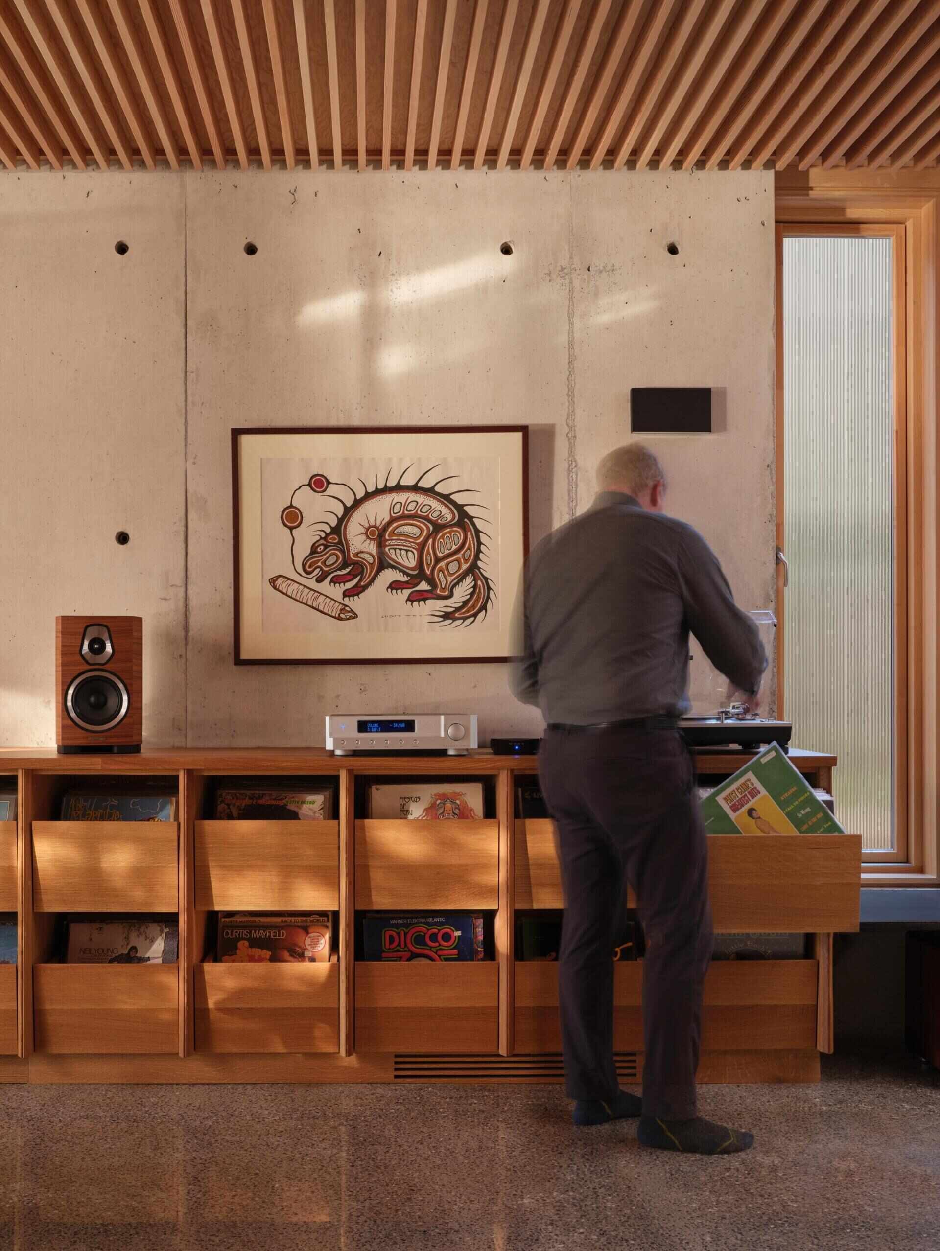 This modern living room opens west toward the lake, framed by millwork cabinets along the wall which house a custom vinyl record storage unit, while a window aligns precisely with the acoustic ceiling, reinforcing the sense that every element has been carefully measured.
