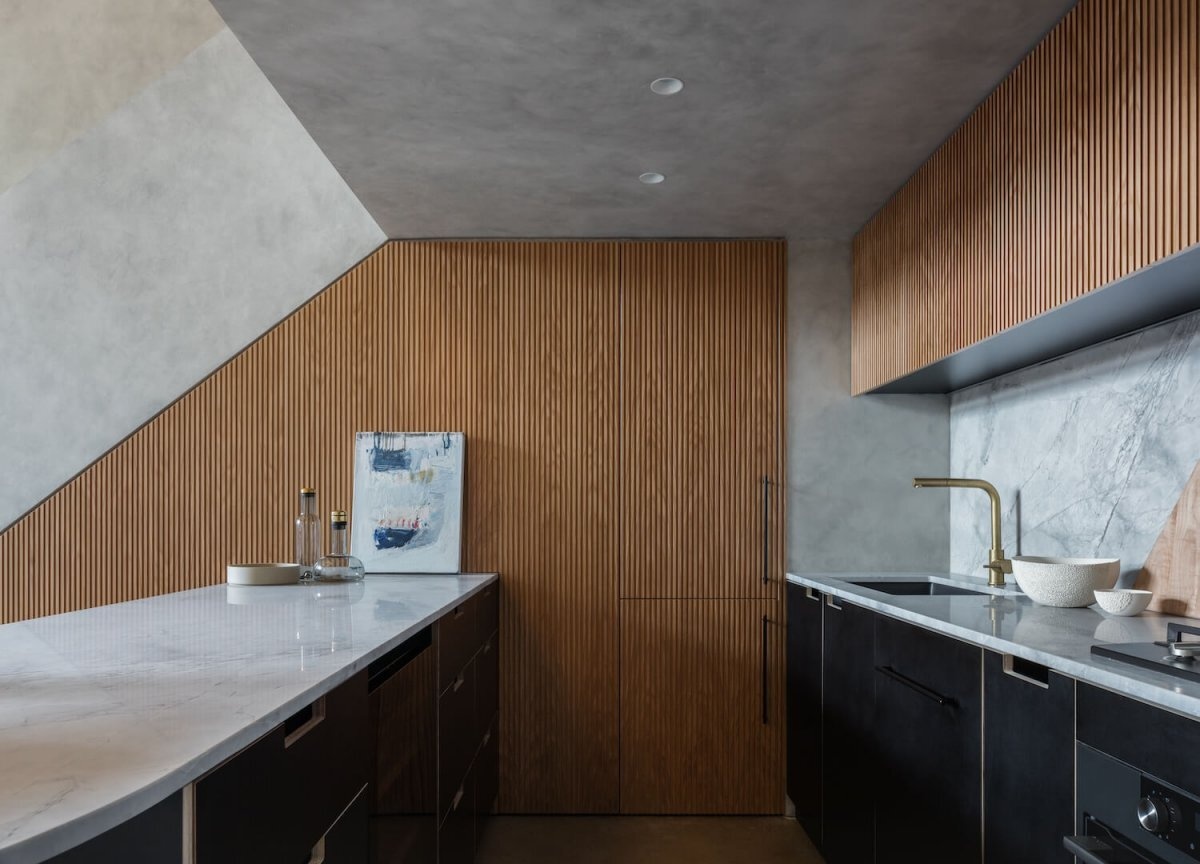 Los detalles inspirados en mediados de siglo, que incluyen carpintería de roble americano, detalles en latón y acabados de madera contrachapada, aportan calidez al loft moderno y oscuro.