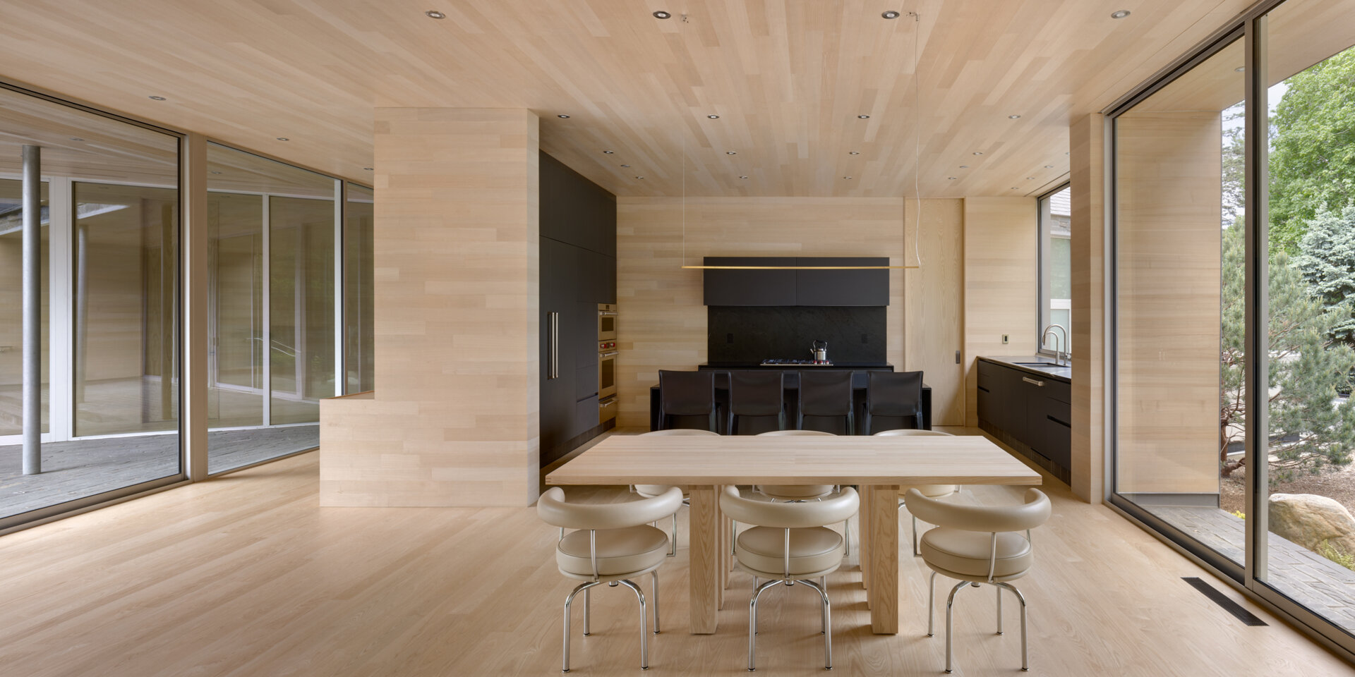 La cocina se integra cómodamente dentro del flujo de la casa, con superficies de madera de fresno blanco que mantienen la continuidad visual, mientras que los gabinetes y encimeras oscuros contrastan con los espacios interiores.