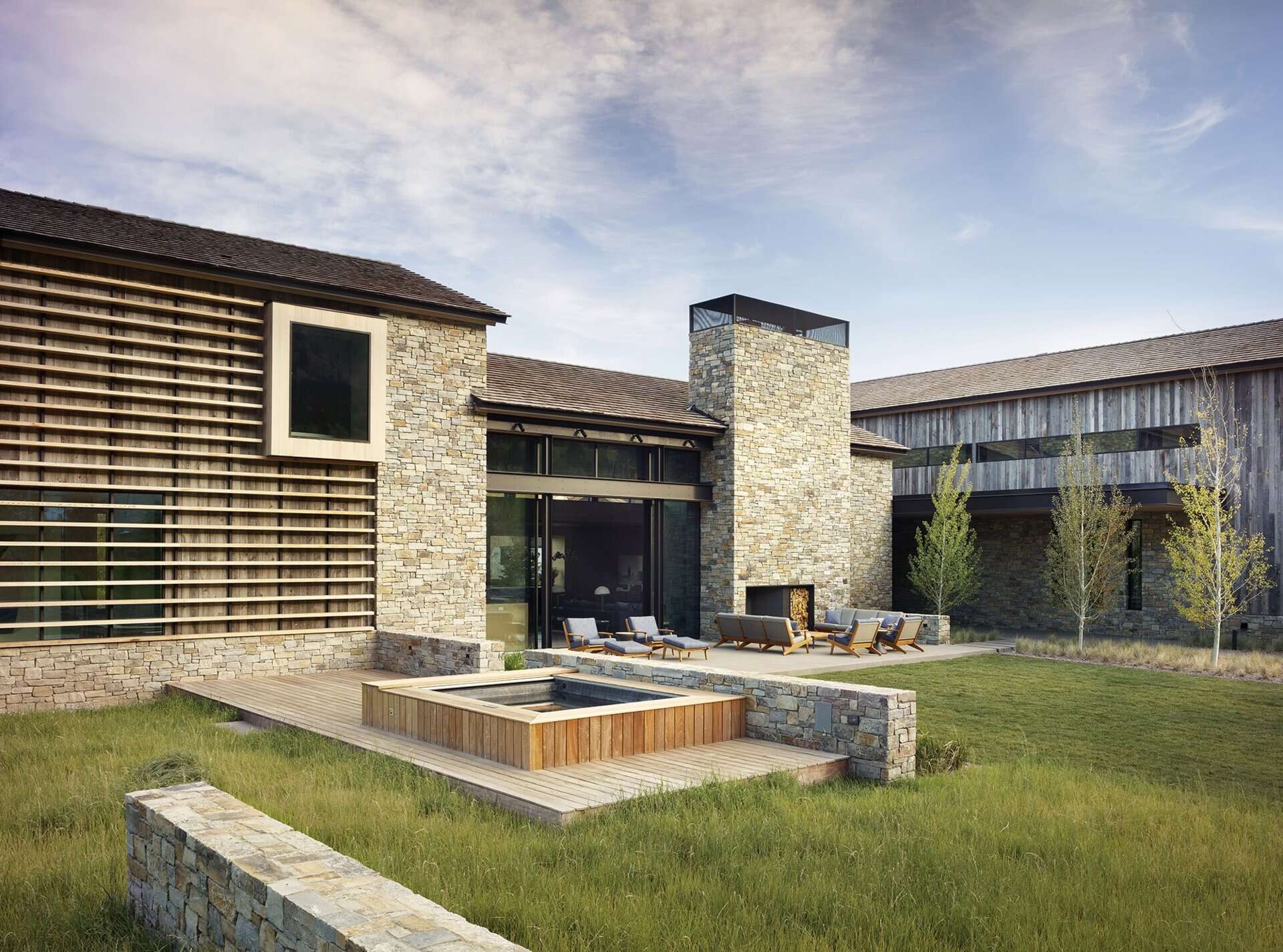 Las puertas corredizas de vidrio se abren a un patio con chimenea al aire libre y bañera de hidromasaje, lo que amplía el espacio habitable hacia las vistas a la montaña.