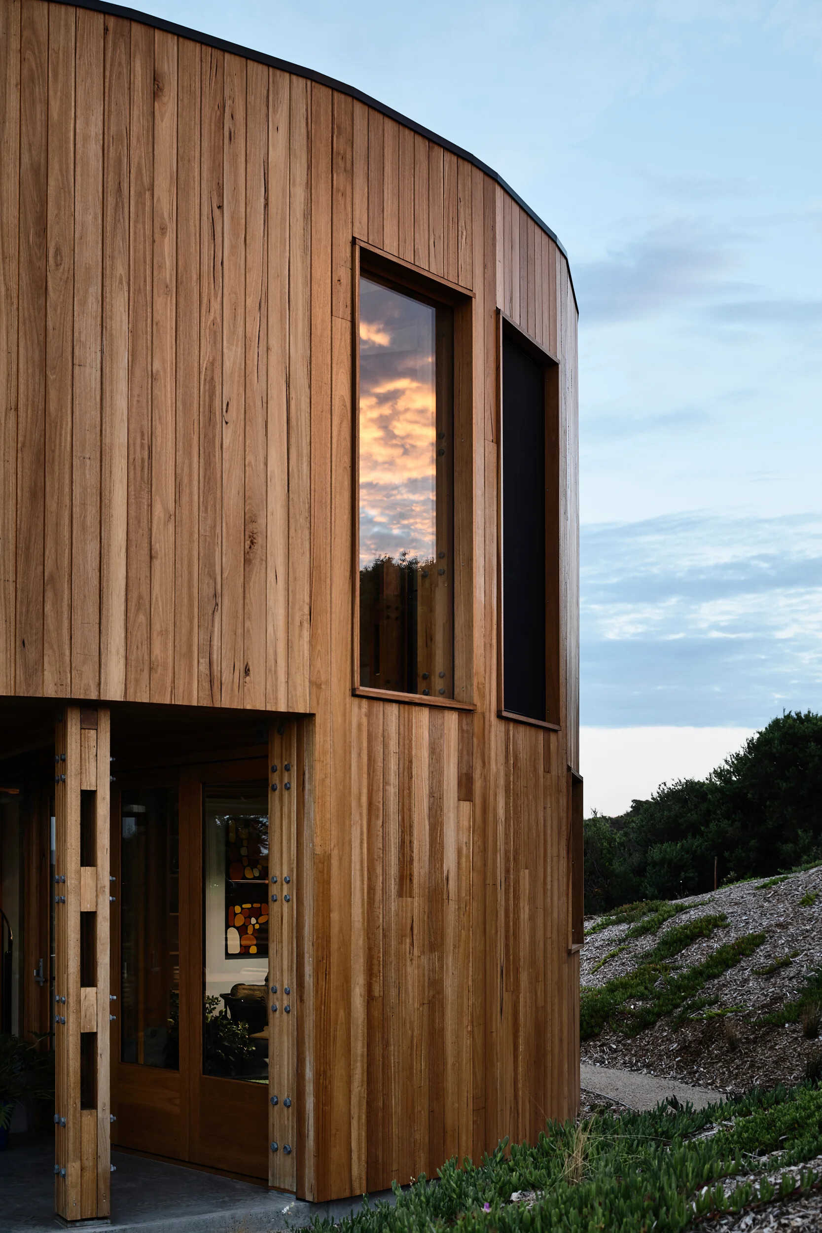 A round beach house with an integrated deck that opens directly to the surrounding sand dunes and bush.