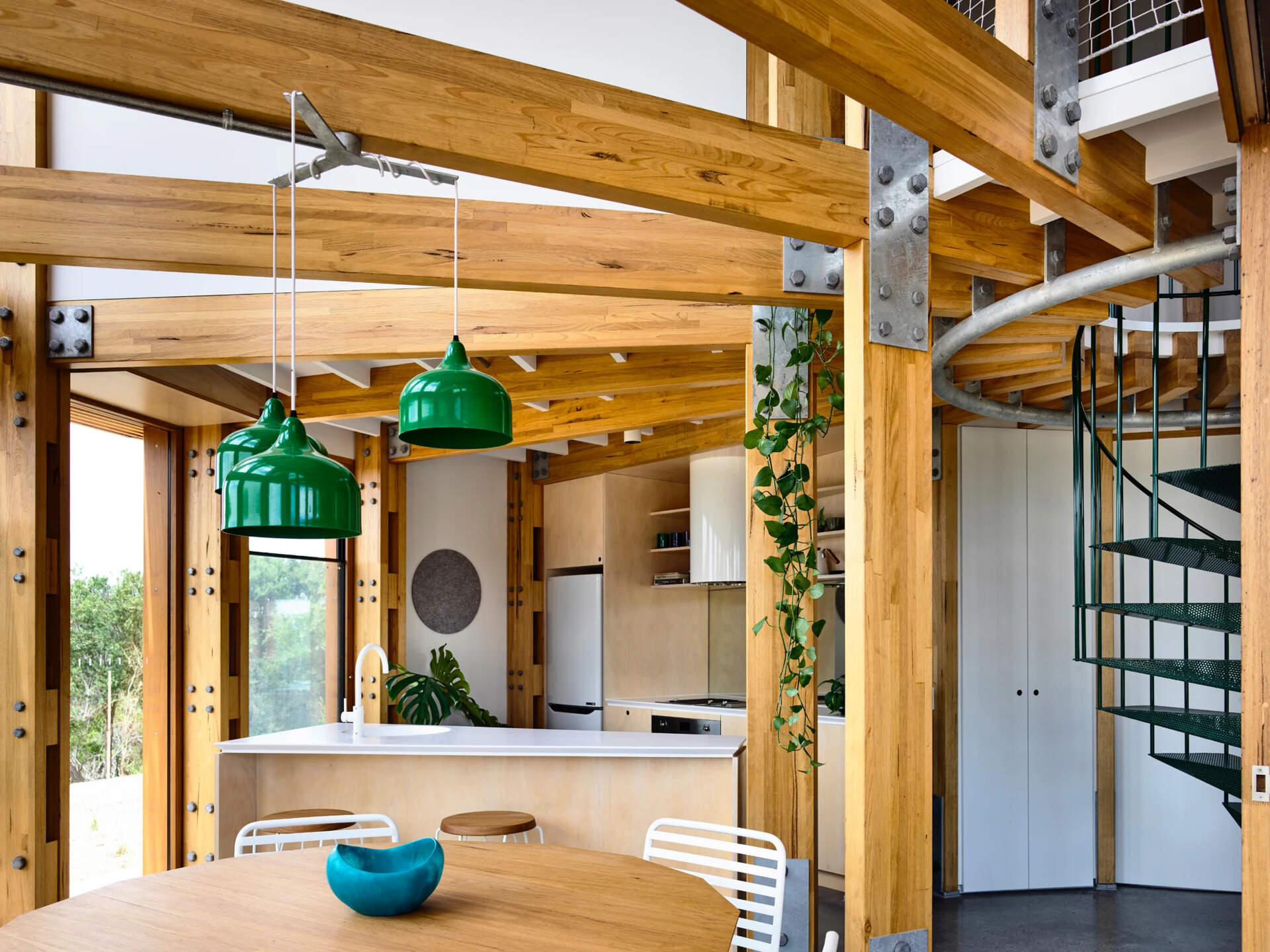 Open plan kitchen, dining and living areas inside a compact circular beach house designed for shared living.