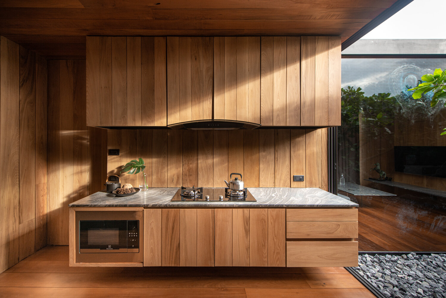Floating wood cabinets define the kitchen, which opens directly onto a small courtyard with a tree at its centre.