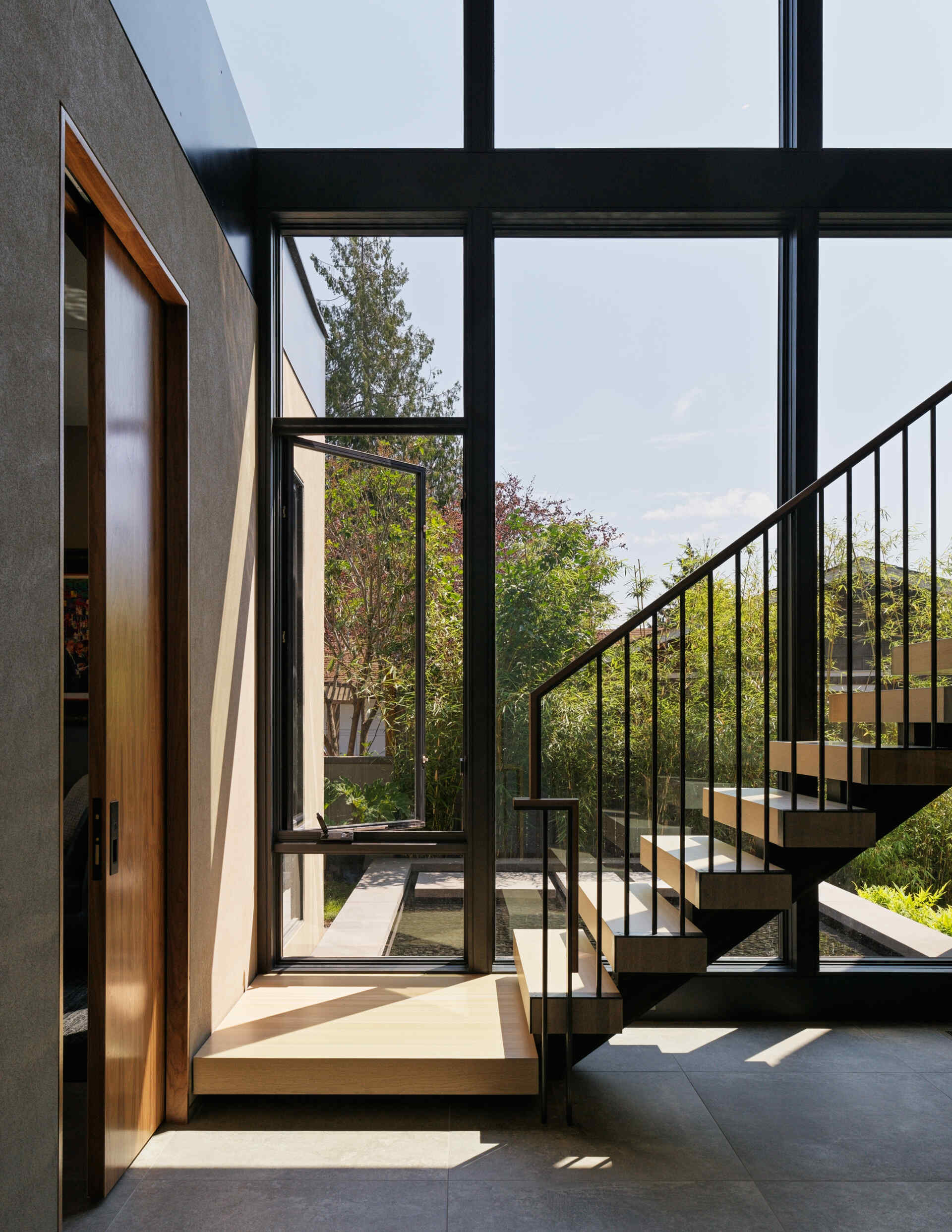 Floating wood-and-steel stairs fill the home with light and flow, acting as a central feature that connects floors and frames views of the pool.