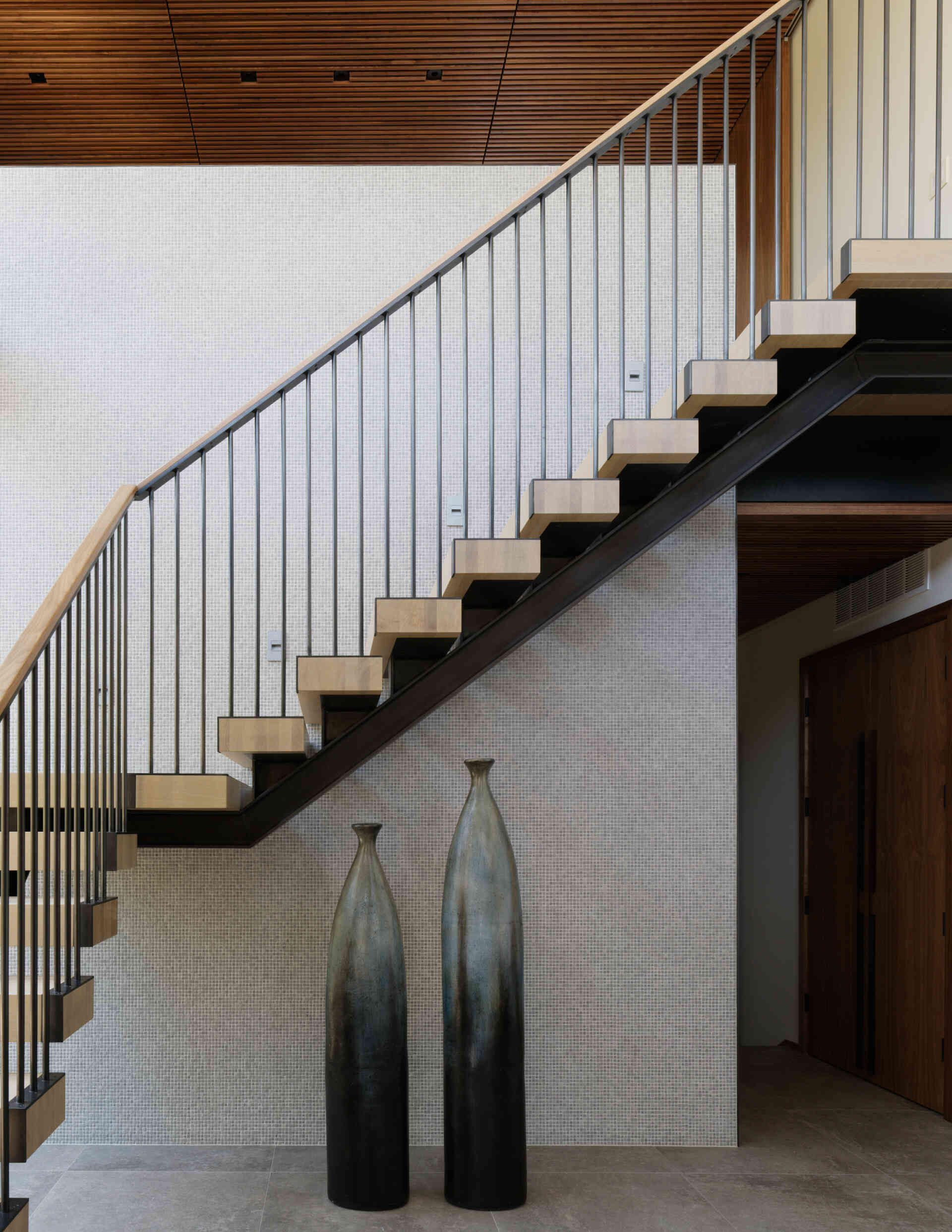 Floating wood-and-steel stairs fill the home with light and flow, acting as a central feature that connects floors and frames views of the pool.