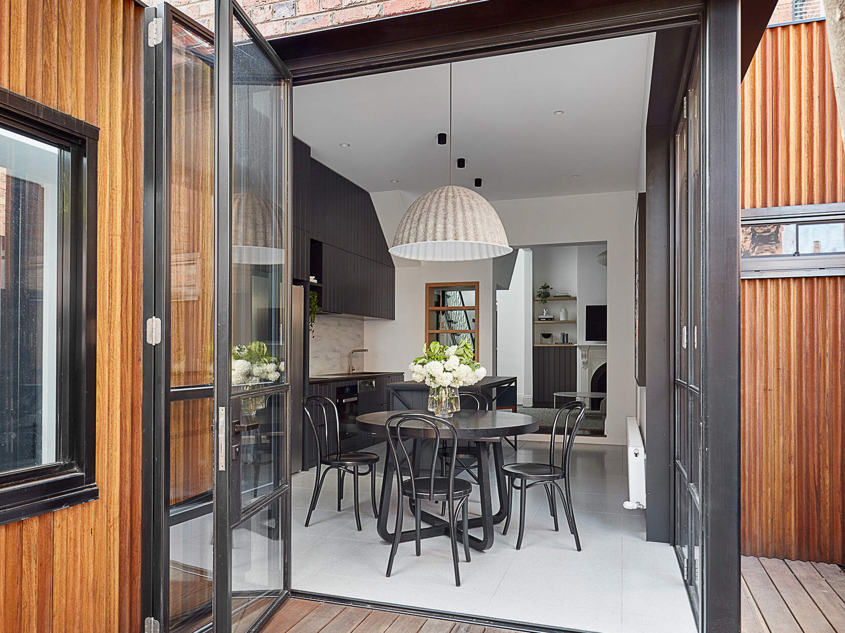 Las puertas plegables de vidrio conectan la cocina y el comedor con el cálido patio de madera y la moderna extensión de madera.