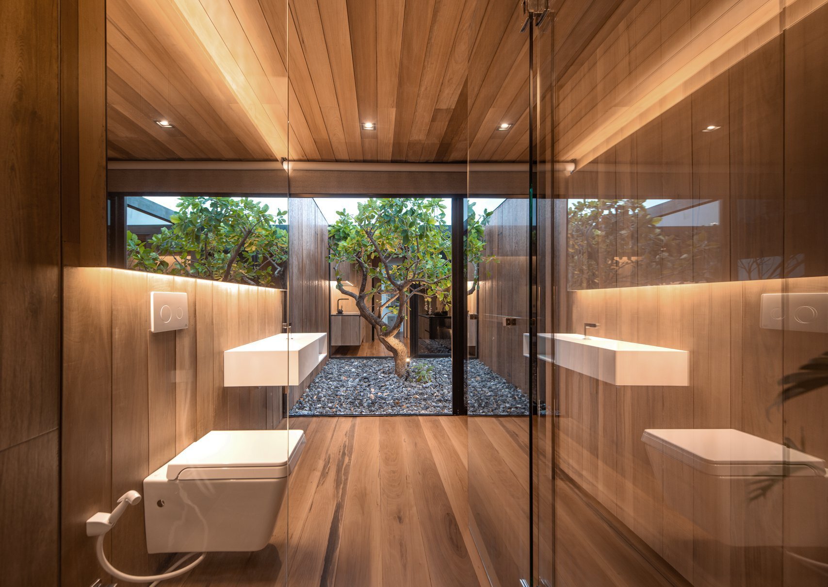 White accents, a backlit mirror, and a full height window bring light into the wood lined bathroom interior.