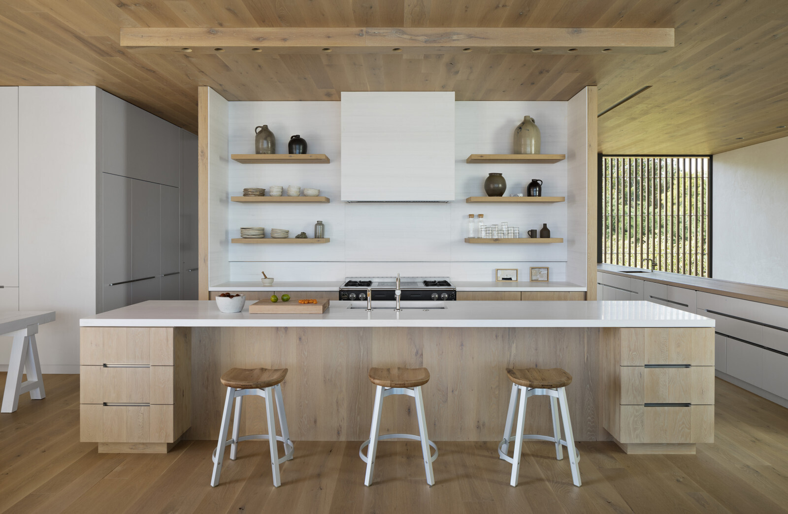 A white kitchen with warm wood accents creates a calm interior at the center of this waterfront home.