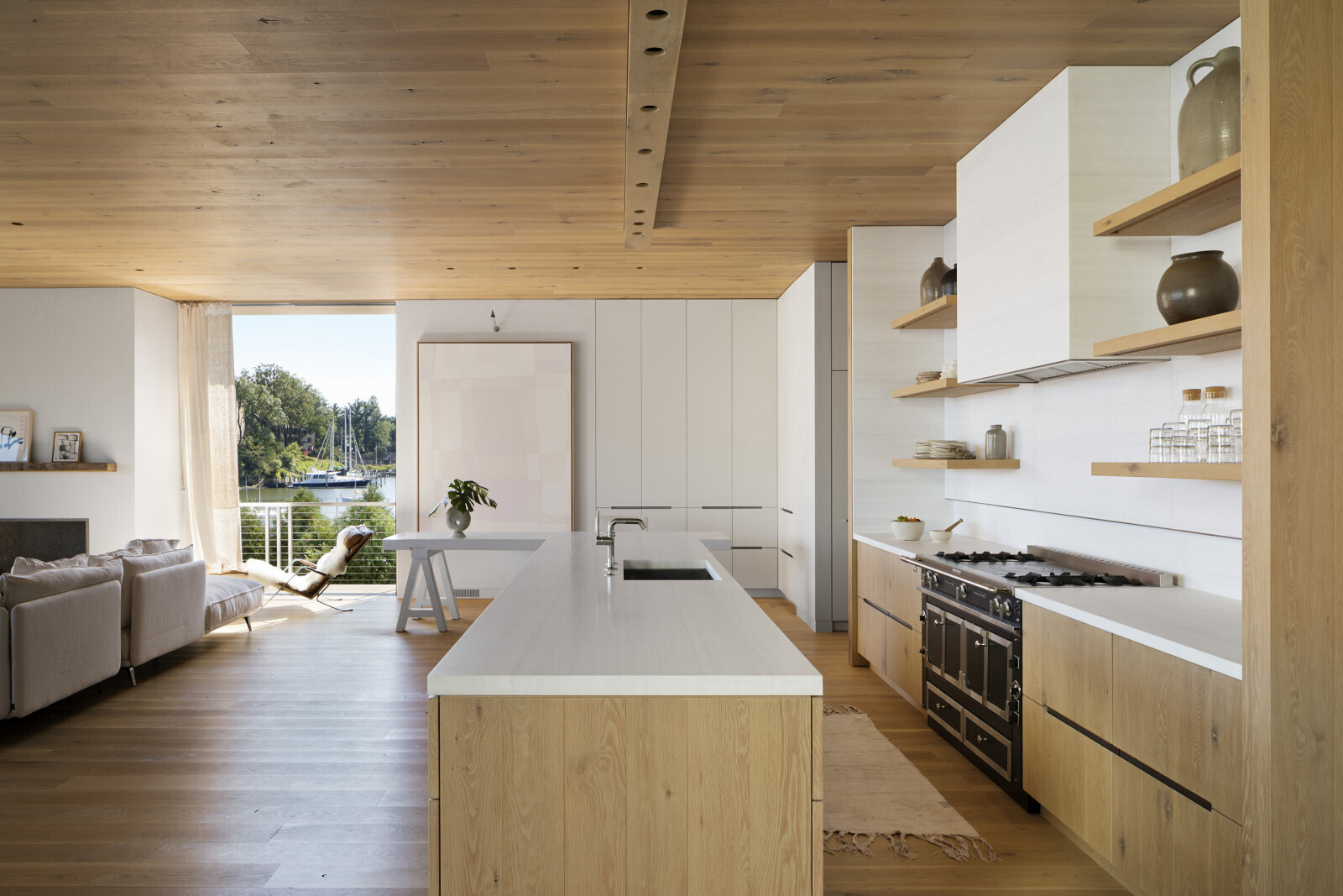 A white kitchen with warm wood accents creates a calm interior at the center of this waterfront home.