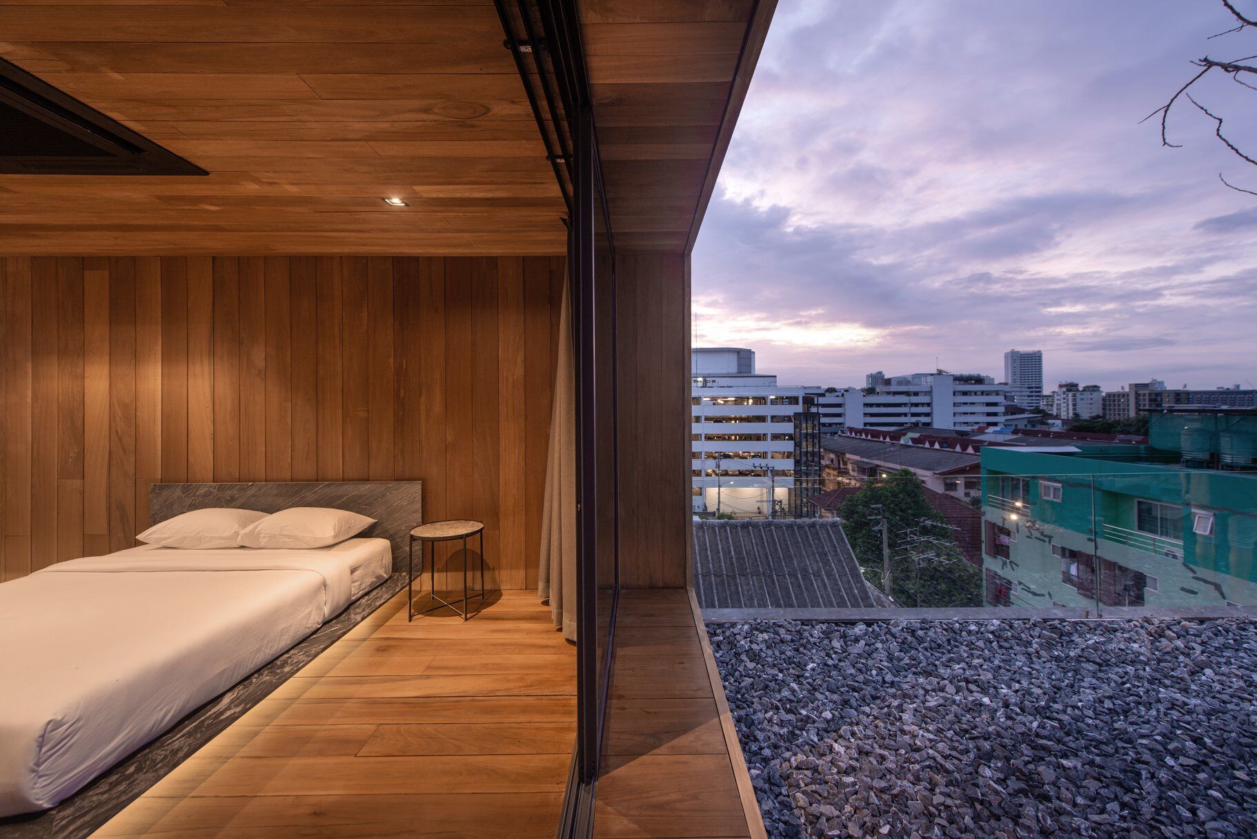 Sliding glass doors connect the bedroom to an outdoor rooftop space finished with pebbles.