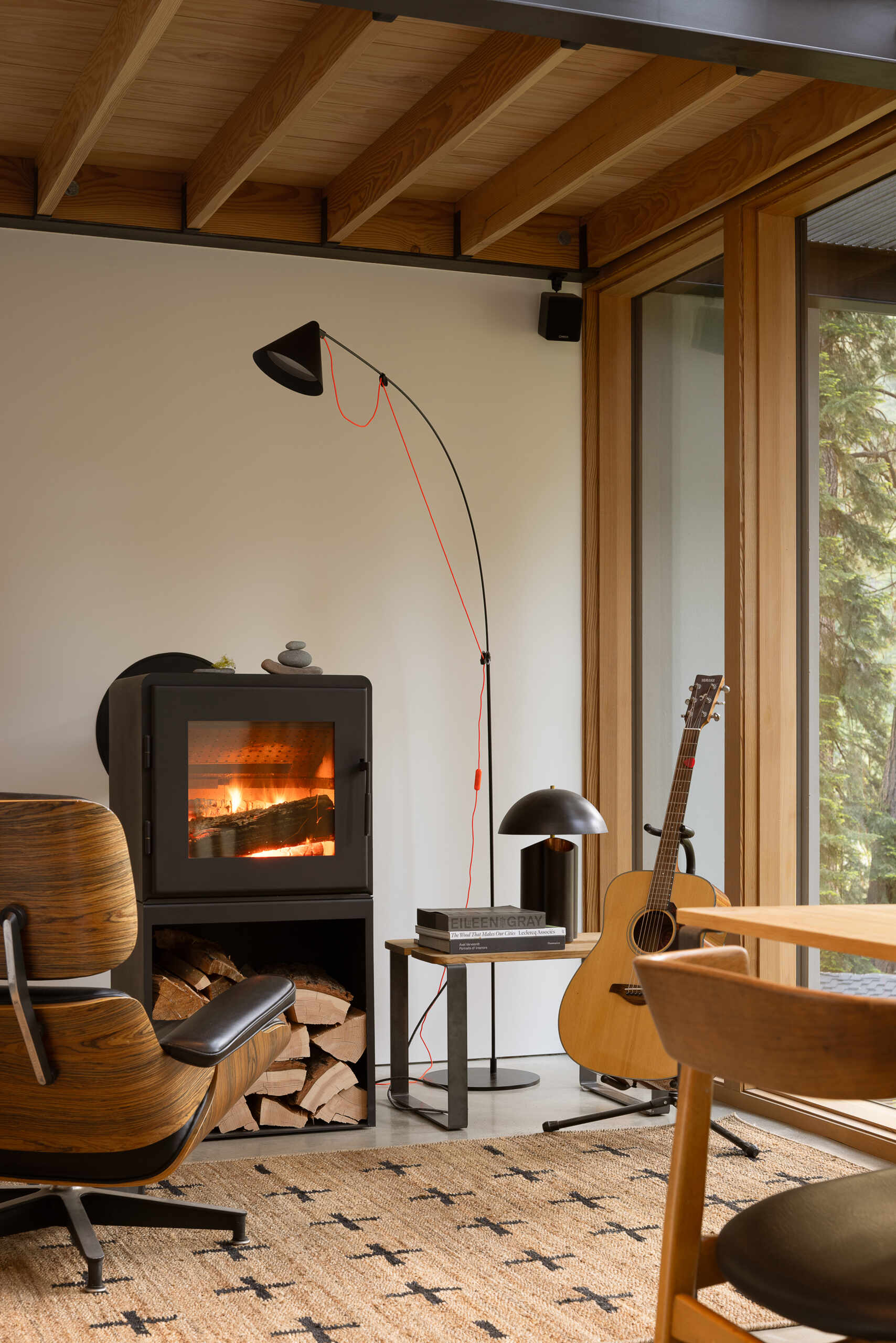 A wood-burning fireplace sits beneath a fir-framed loft, adding warmth and focus to the room. Throughout the level, interior finishes remain minimal, creating a calm backdrop for shifting light, artwork, and views into the surrounding forest.