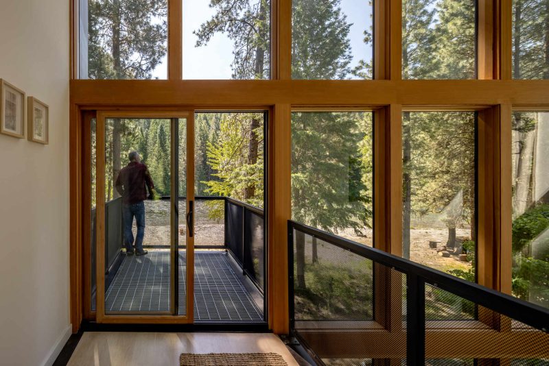 At the top level of a cabin, a loft opens to a cantilevered steel deck. Constructed from galvanized metal decking, the lookout deck extends the living space outward and upward, offering elevated views through the trees and toward the river.