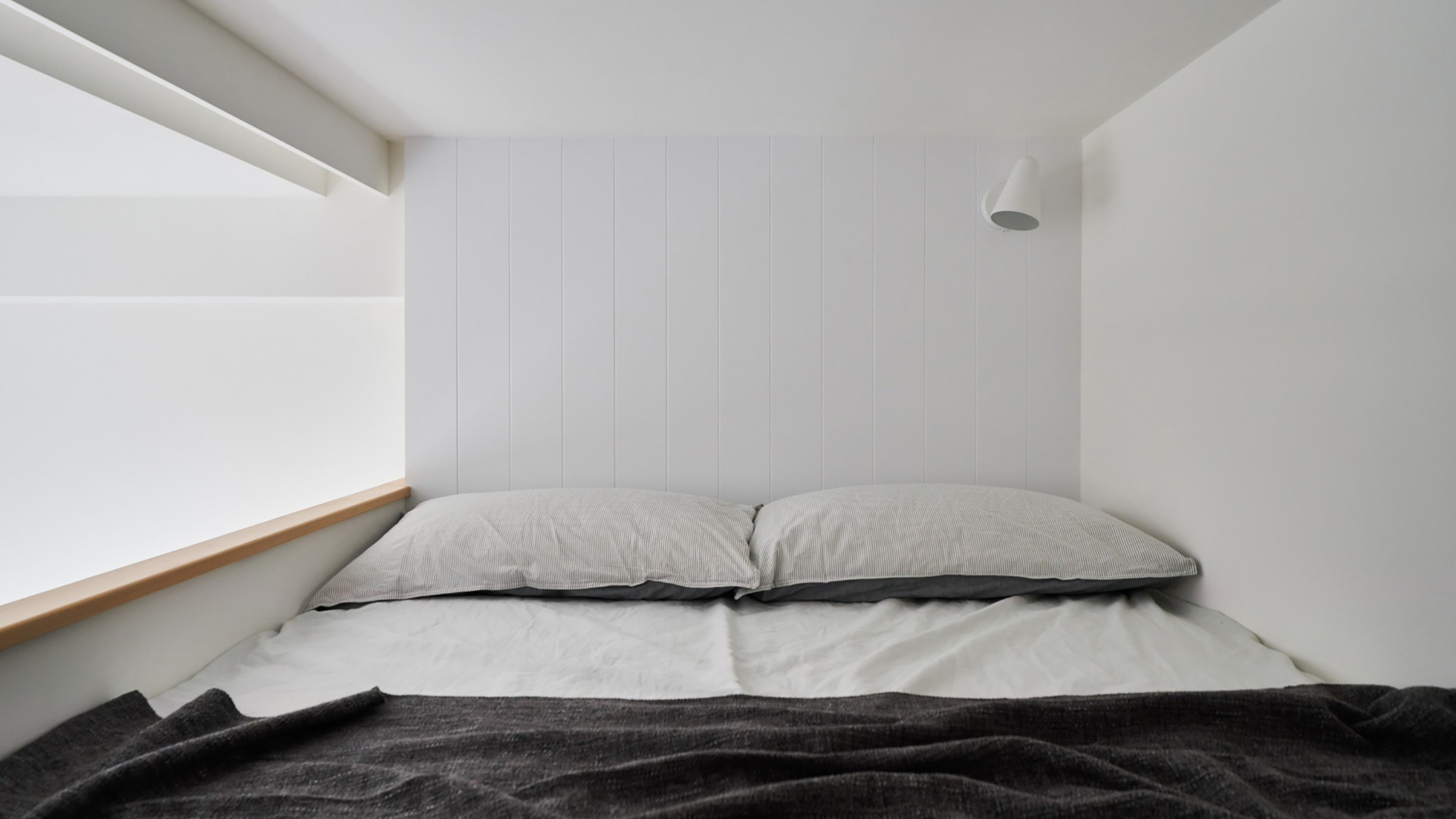 A minimalist loft bedroom crowns this tiny Taipei apartment, featuring built in shelving and a clean headboard wall for a calm sleeping zone.