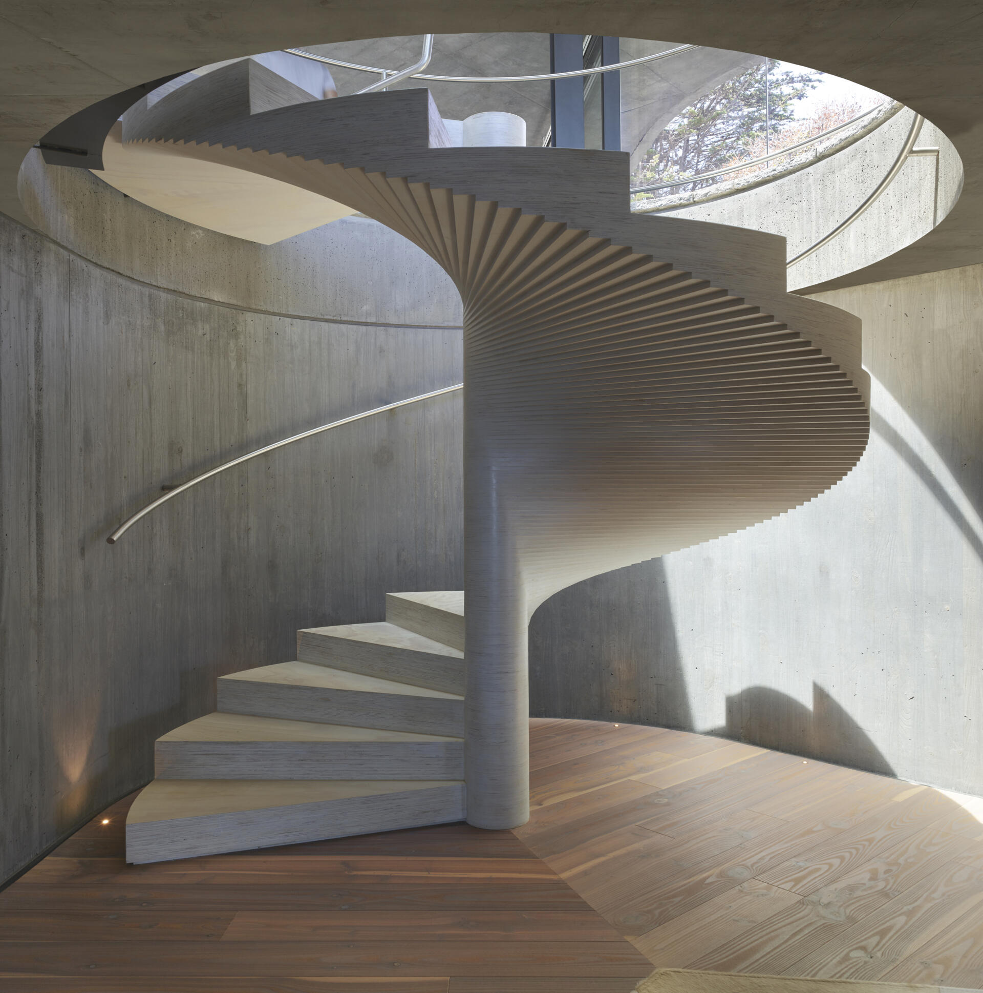 A sculptural spiral staircase made from stacked plywood connects the pavilion to the lower level.