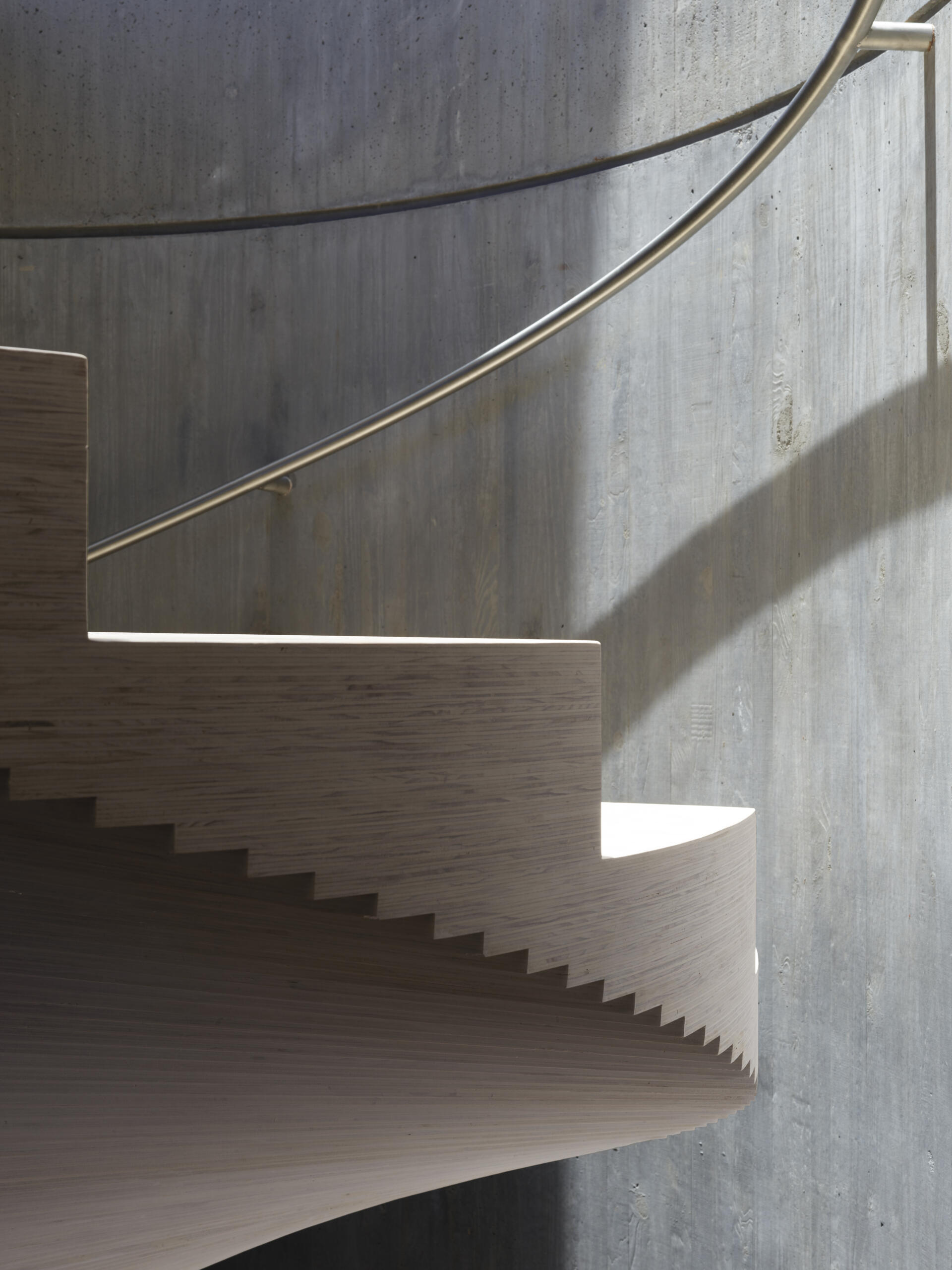A sculptural spiral staircase made from stacked plywood connects the pavilion to the lower level.