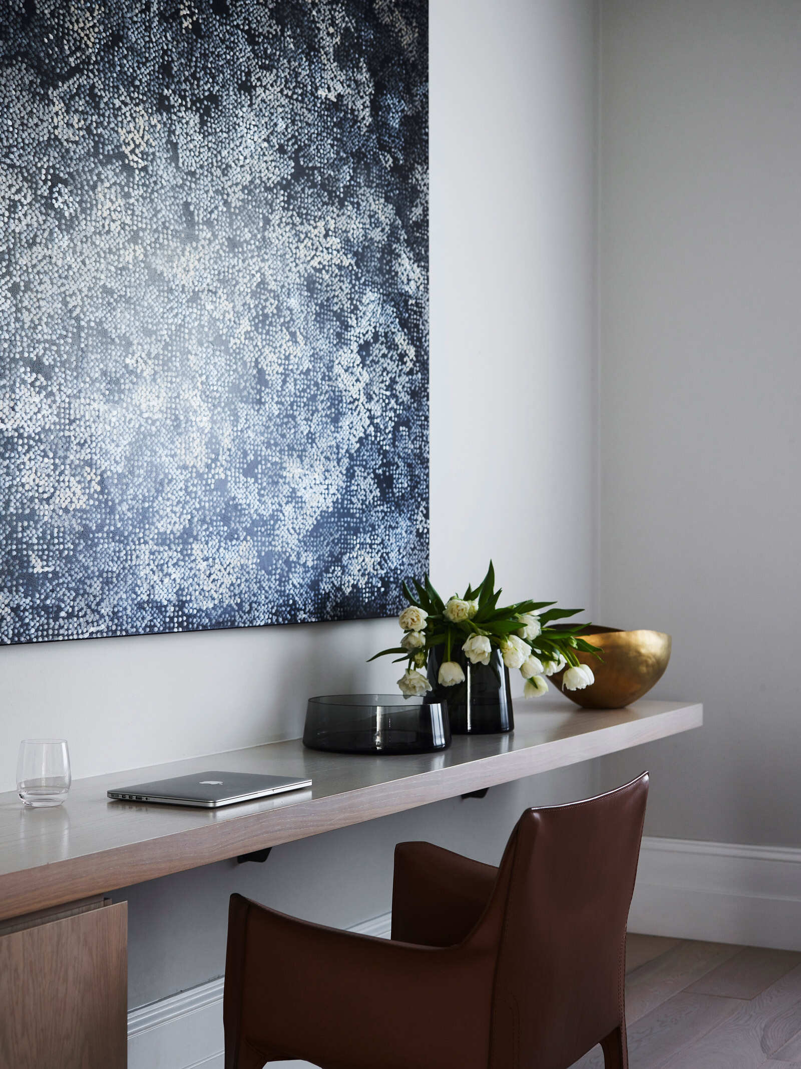 Una oficina en casa llena de luz diseñada para exhibir arte en un interior neutro.