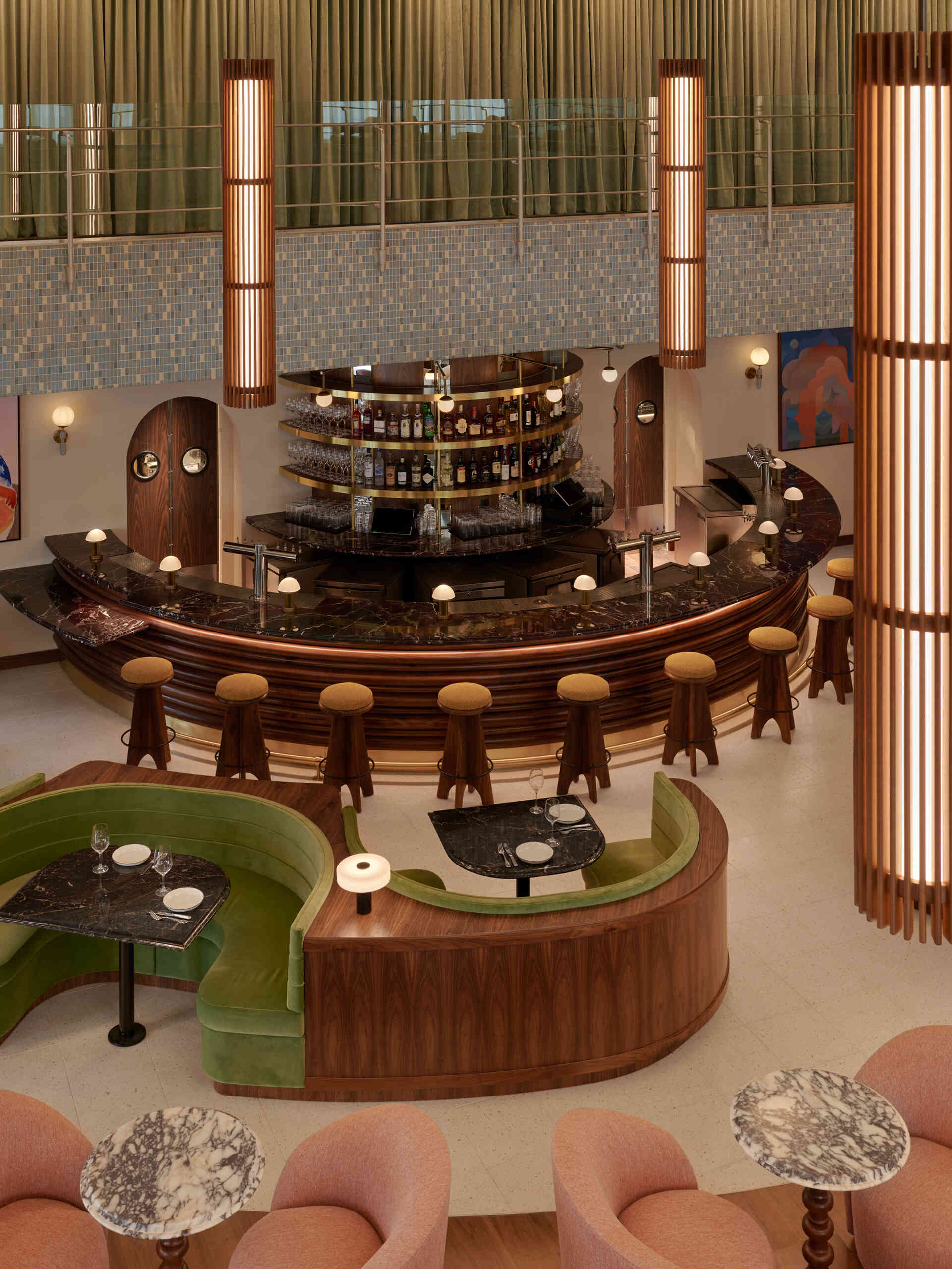A double heighthotel lobby centers on a sculptural semicircular bar, where restored mosaic tile and mid-century lighting set the tone for gathering.