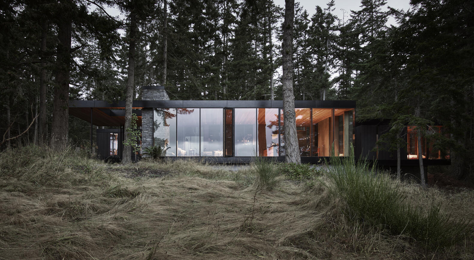 A modern farmhouse tucked into a forested hillside on Whidbey Island, overlooking barns, cattle fields and a pond. Warm wood and stone connect the home to its agricultural surroundings.