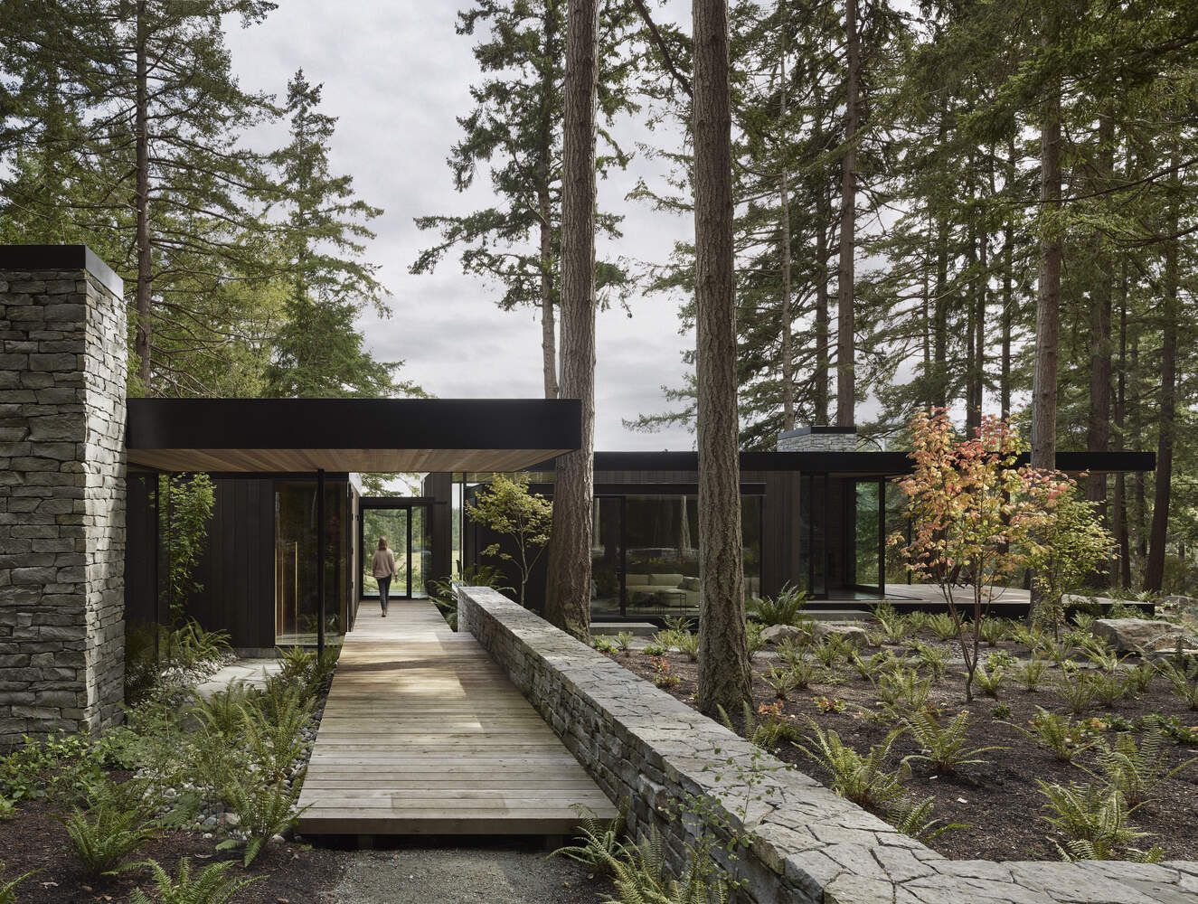 A modern farmhouse tucked into a forested hillside on Whidbey Island, overlooking barns, cattle fields and a pond. Warm wood and stone connect the home to its agricultural surroundings.