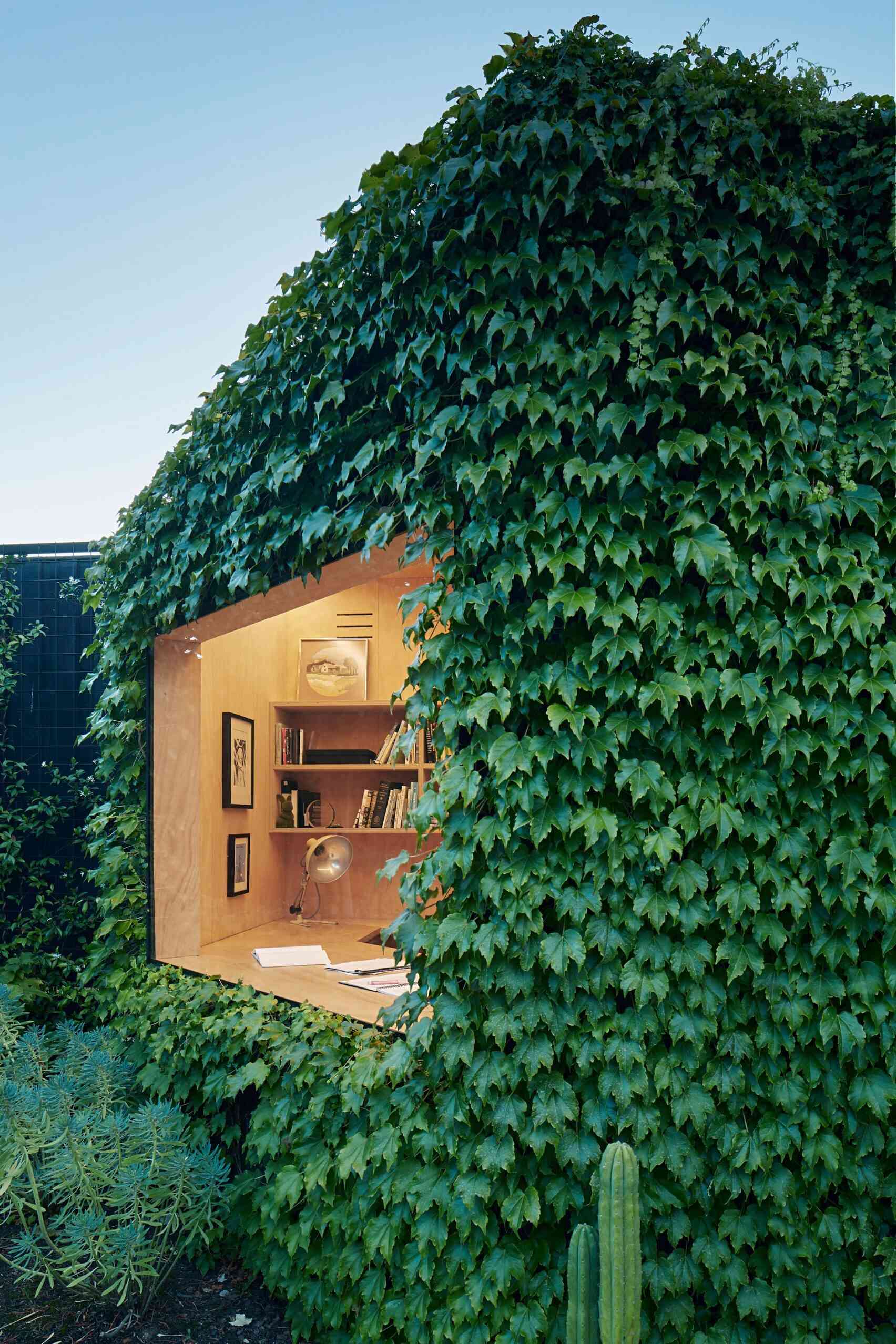 This ivy covered backyard cabin in Melbourne is a compact, peaceful workspace for creative writing. Blending seamlessly into a leafy garden, it features a plywood interior, large picture window, skylight, and sustainable design elements, offering an inspiring retreat just steps from home.