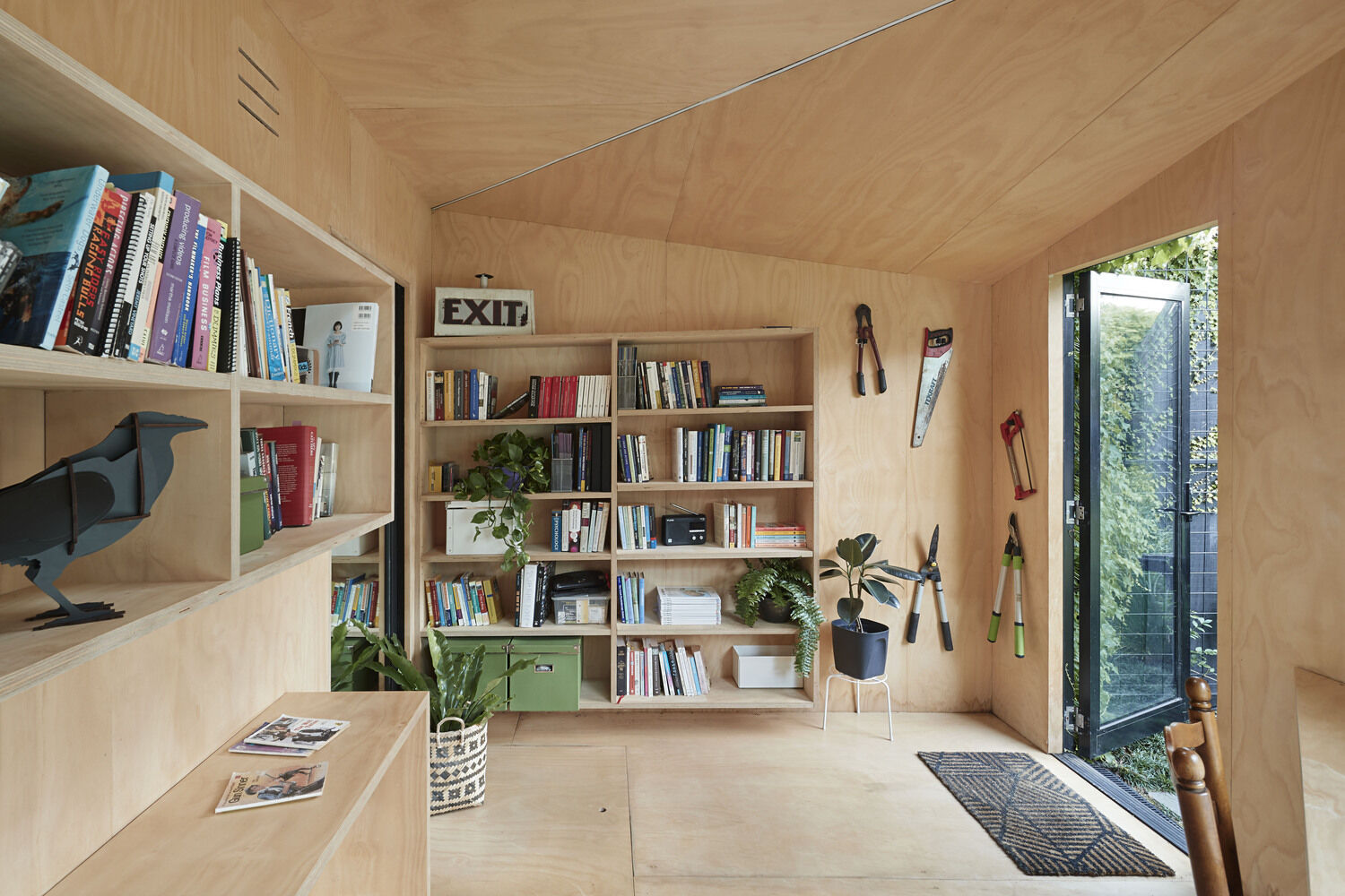 This ivy covered backyard cabin in Melbourne is a compact, peaceful workspace for creative writing. Blending seamlessly into a leafy garden, it features a plywood interior, large picture window, skylight, and sustainable design elements, offering an inspiring retreat just steps from home.